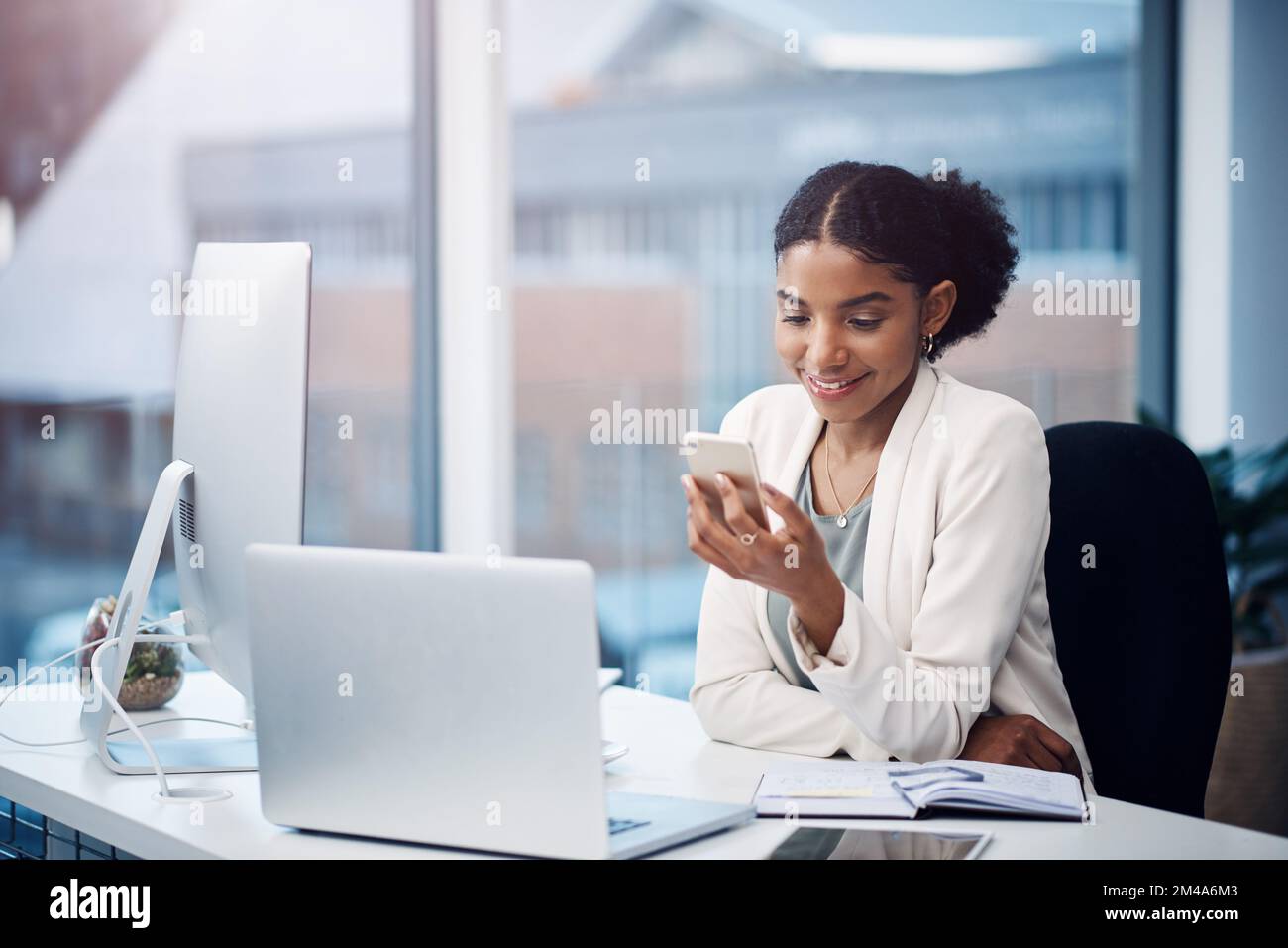 Nella zona Get IT Done (operazioni eseguite). una giovane donna d'affari che utilizza un telefono cellulare alla sua scrivania in un ufficio moderno. Foto Stock