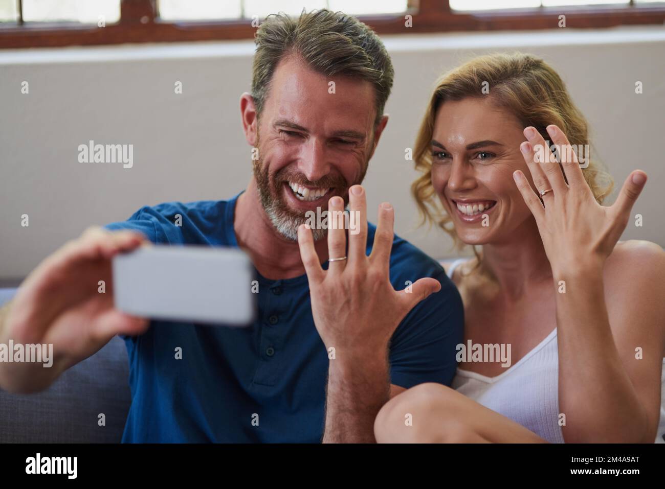 Il primo di tanti ricordi come coppia sposata. una coppia felice di mezza età che prende un selfie e che mostra fuori i loro anelli di nozze a casa. Foto Stock