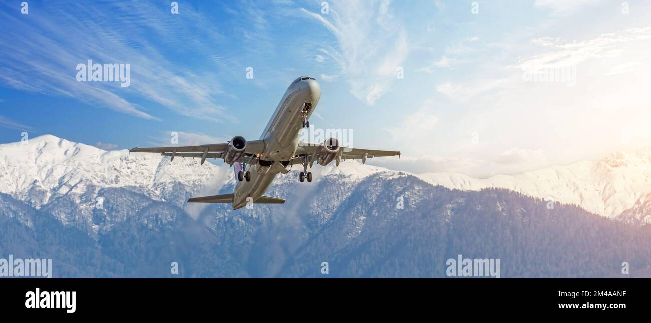 Gli aerei civili passeggeri decolgono sullo sfondo di enormi montagne innevate. Formato banner panoramico a visualizzazione ampia Foto Stock