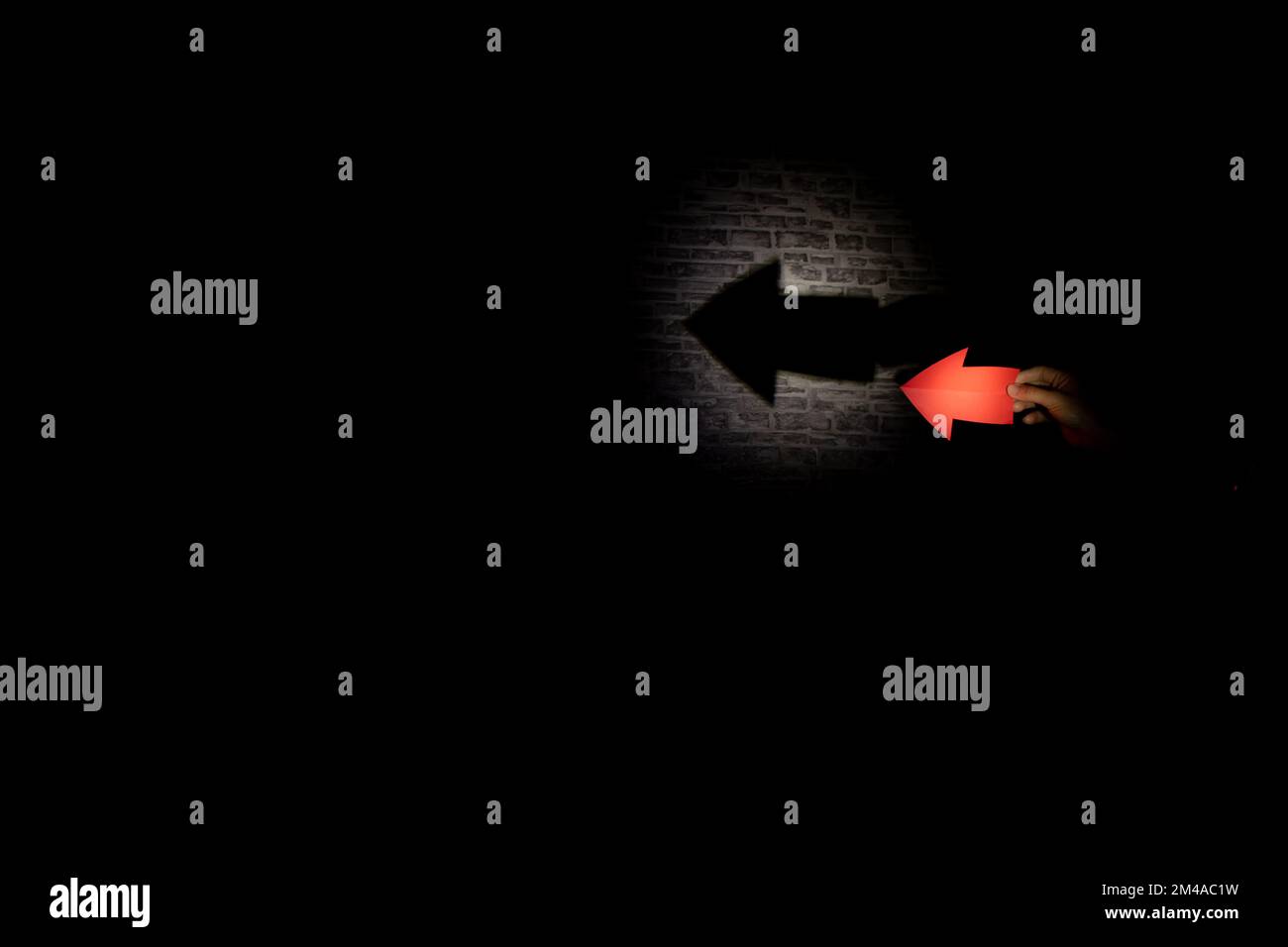 freccia su carta illuminata da una lanterna crea un'ombra di una freccia su uno sfondo scuro Foto Stock
