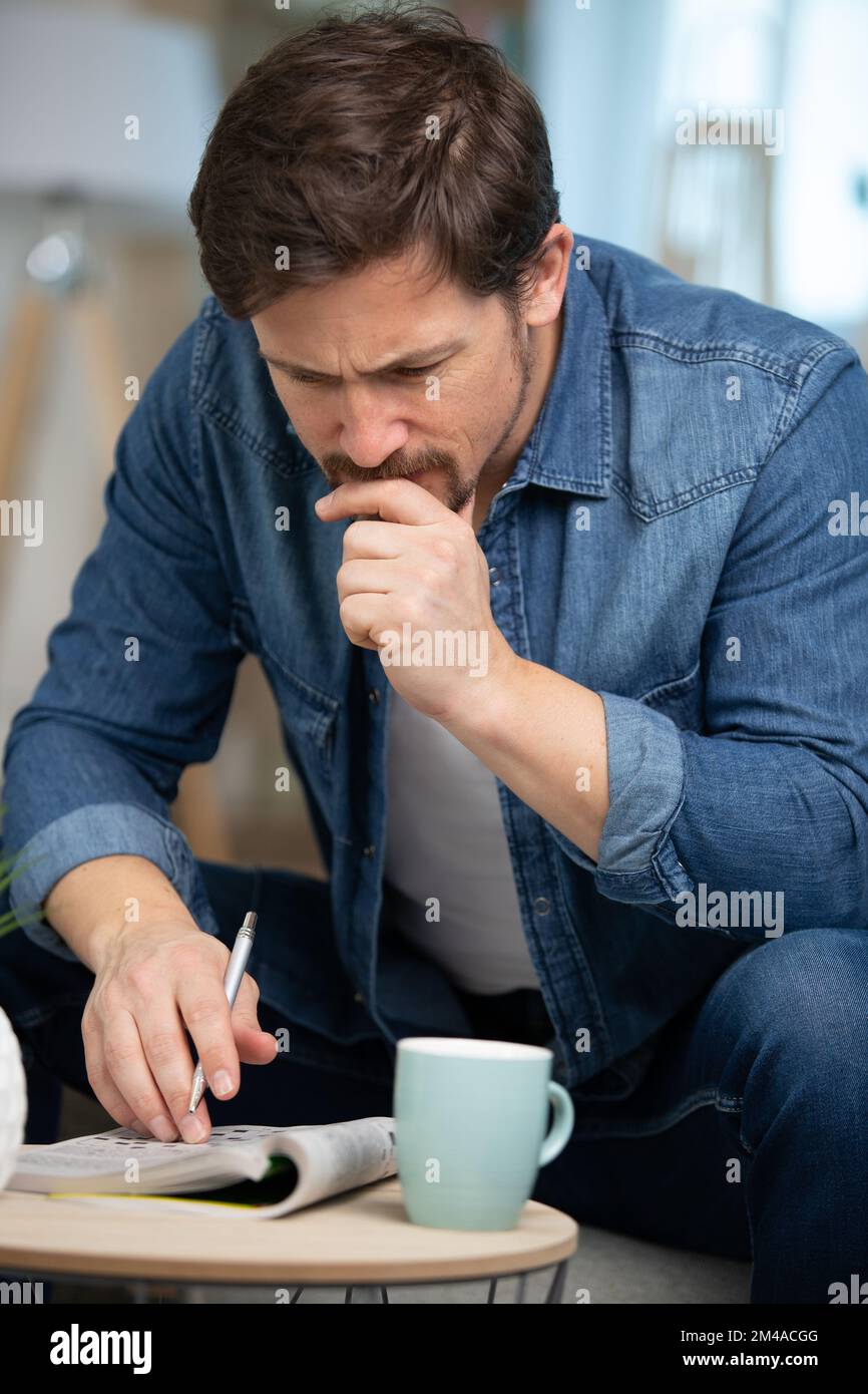 giovane uomo seduto facendo un puzzle crossword Foto Stock