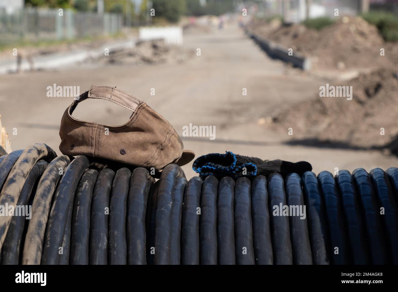 il cappello da baseball e i guanti da costruzione giacciono su un cavo nero lasciato dal costruttore al sole Foto Stock