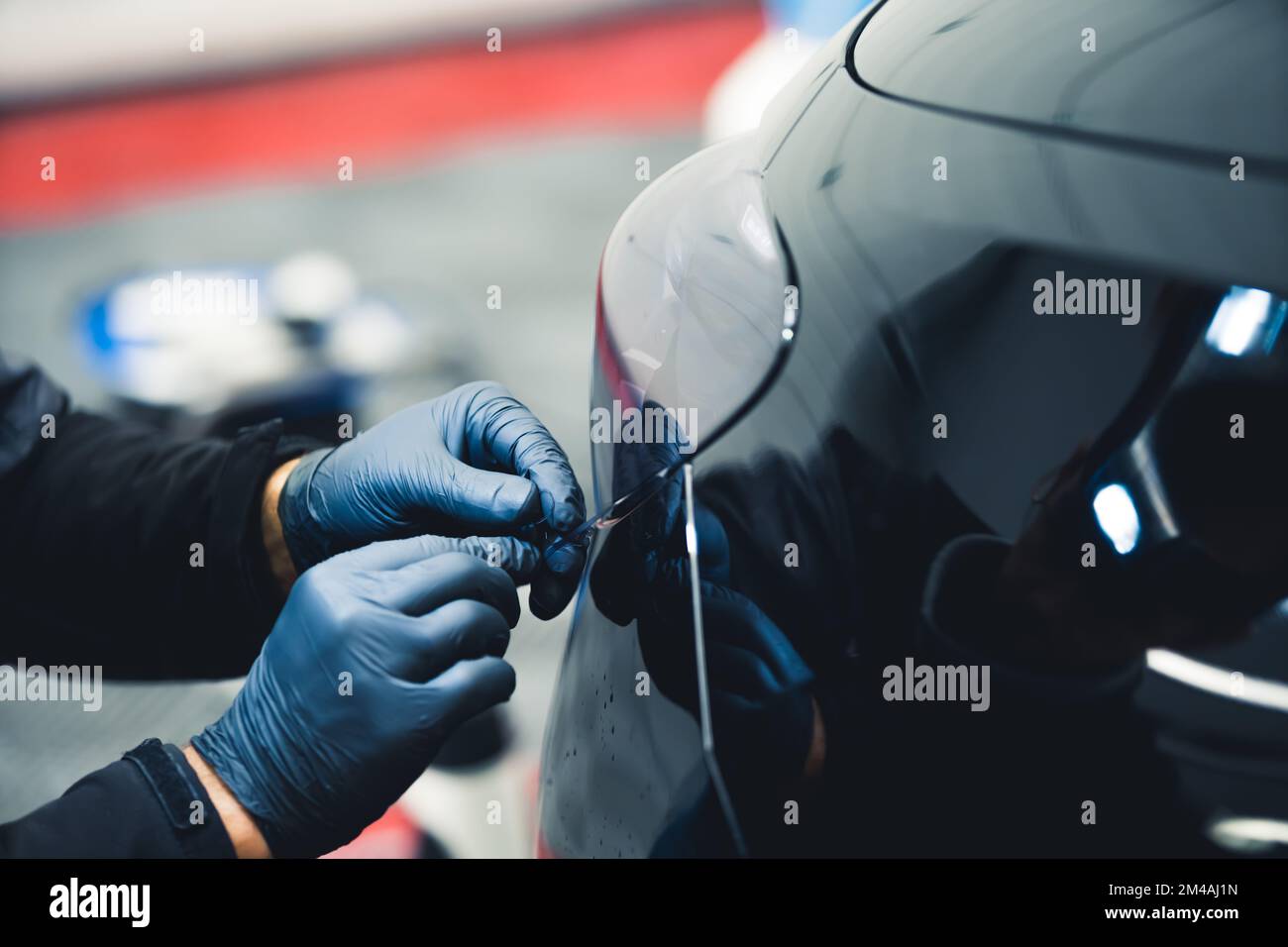 Primo piano di una persona che indossa guanti blu che lavora sulla luce di coda di un'auto nera in un garage. Dettagli dell'auto. Ripresa orizzontale da interno . Foto di alta qualità Foto Stock