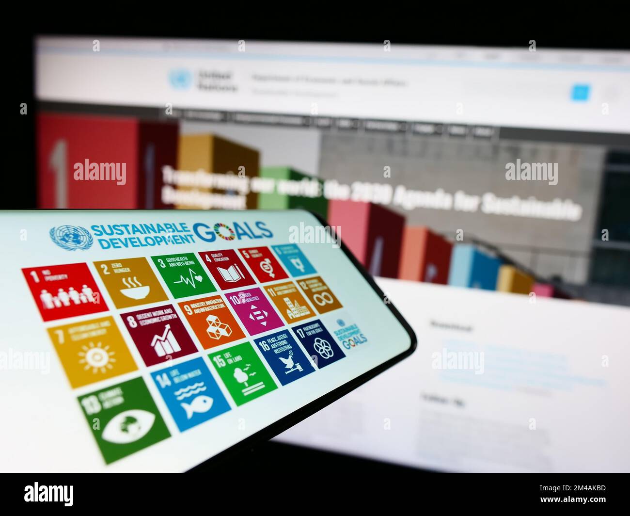 Smartphone con il logo degli obiettivi di sviluppo sostenibile delle Nazioni Unite (SDG) sullo schermo di fronte al sito Web. Messa a fuoco al centro a destra del display del telefono. Foto Stock