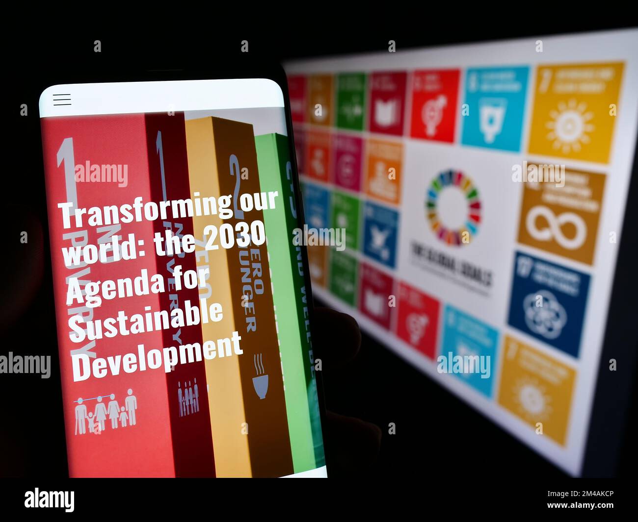 Persona che tiene il cellulare con il sito web degli obiettivi di sviluppo sostenibile delle Nazioni Unite (SDG) sullo schermo di fronte al logo. Messa a fuoco al centro del display del telefono. Foto Stock
