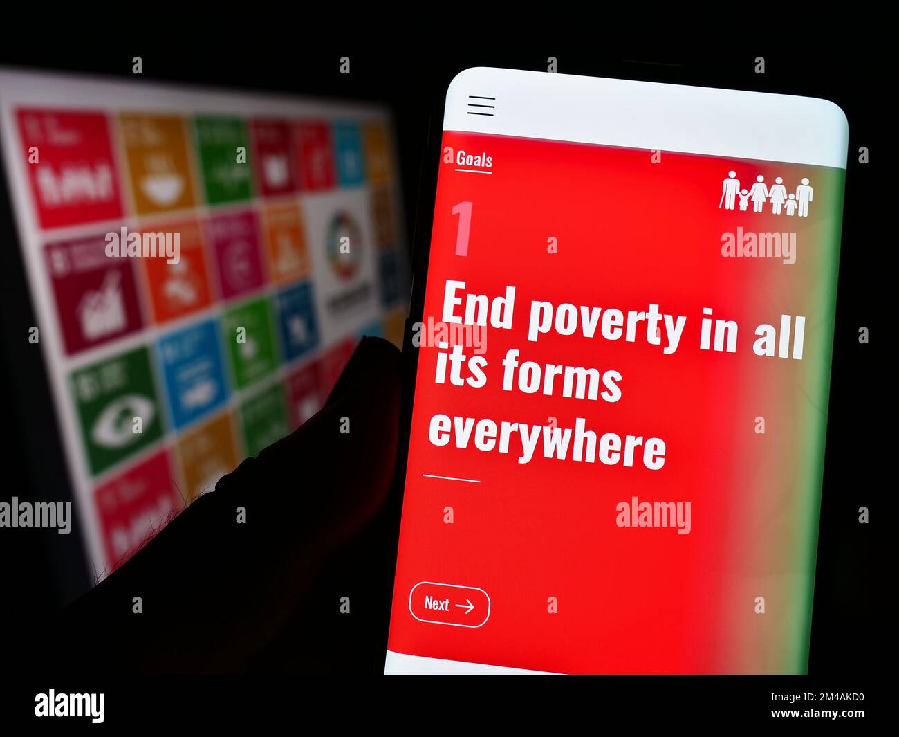 Persona che tiene in mano uno smartphone con la pagina Web degli obiettivi di sviluppo sostenibile delle Nazioni Unite (SDG) sullo schermo davanti al logo. Messa a fuoco sul centro del display. Foto Stock