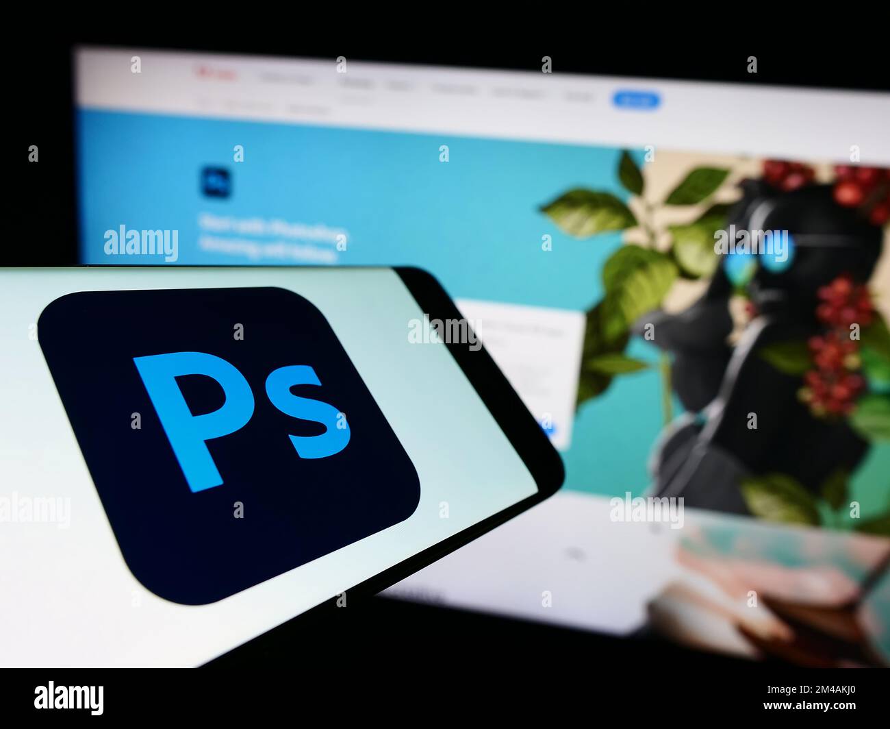 Telefono cellulare con il logo del software editor di grafica Adobe Photoshop sullo schermo di fronte al sito web aziendale. Messa a fuoco al centro del display del telefono. Foto Stock