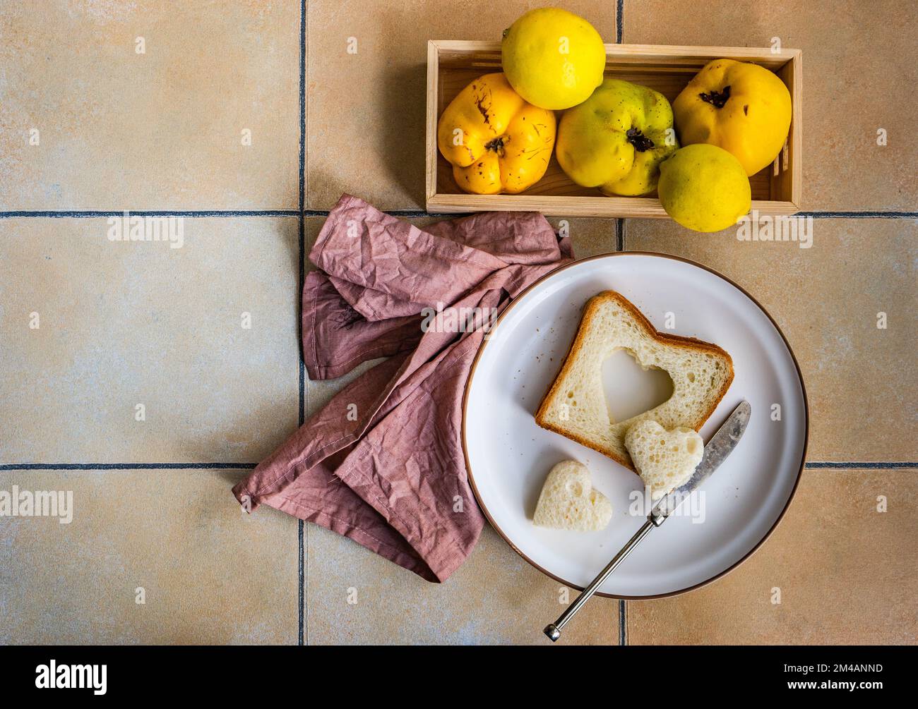 Dal piatto superiore con fette di pane tostato e taglio a forma di cuore e scatola con frutta di mela cotogna strappata in scatola di legno Foto Stock