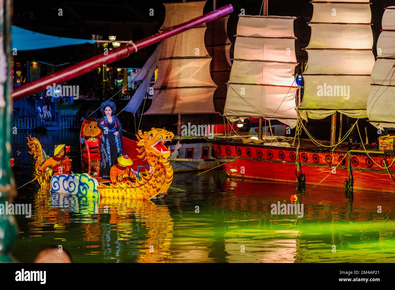 Sul fiume Thu Bon con una signora drago della barca a file che corre a riva accanto a vecchie navi a vela. Foto Stock