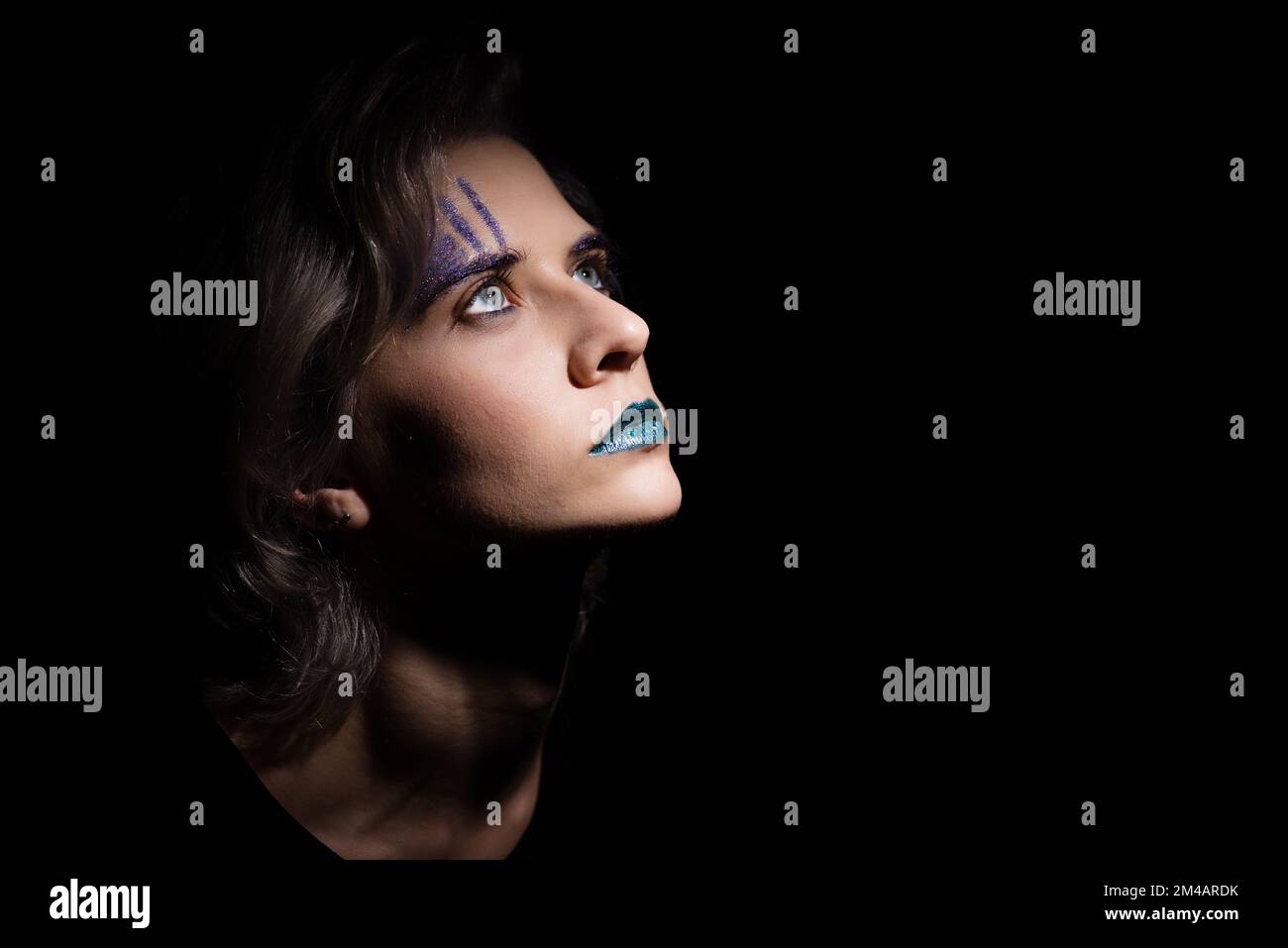 ritratto femminile scuro drammatico con trucco di colore teal trendy. donna bionda capelli che guarda in alto, misterioso ritratto di donna su sfondo scuro Foto Stock
