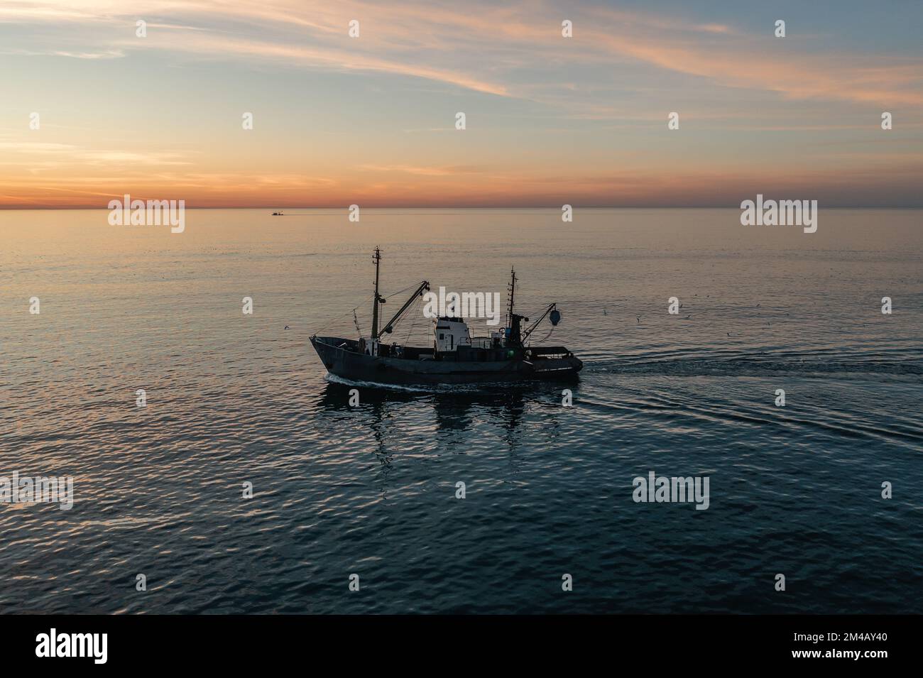 Barca da pesca cattura il pesce al tramonto vista aerea dal drone. Piccola nave da pesca a strascico sulla superficie del mare. Foto Stock