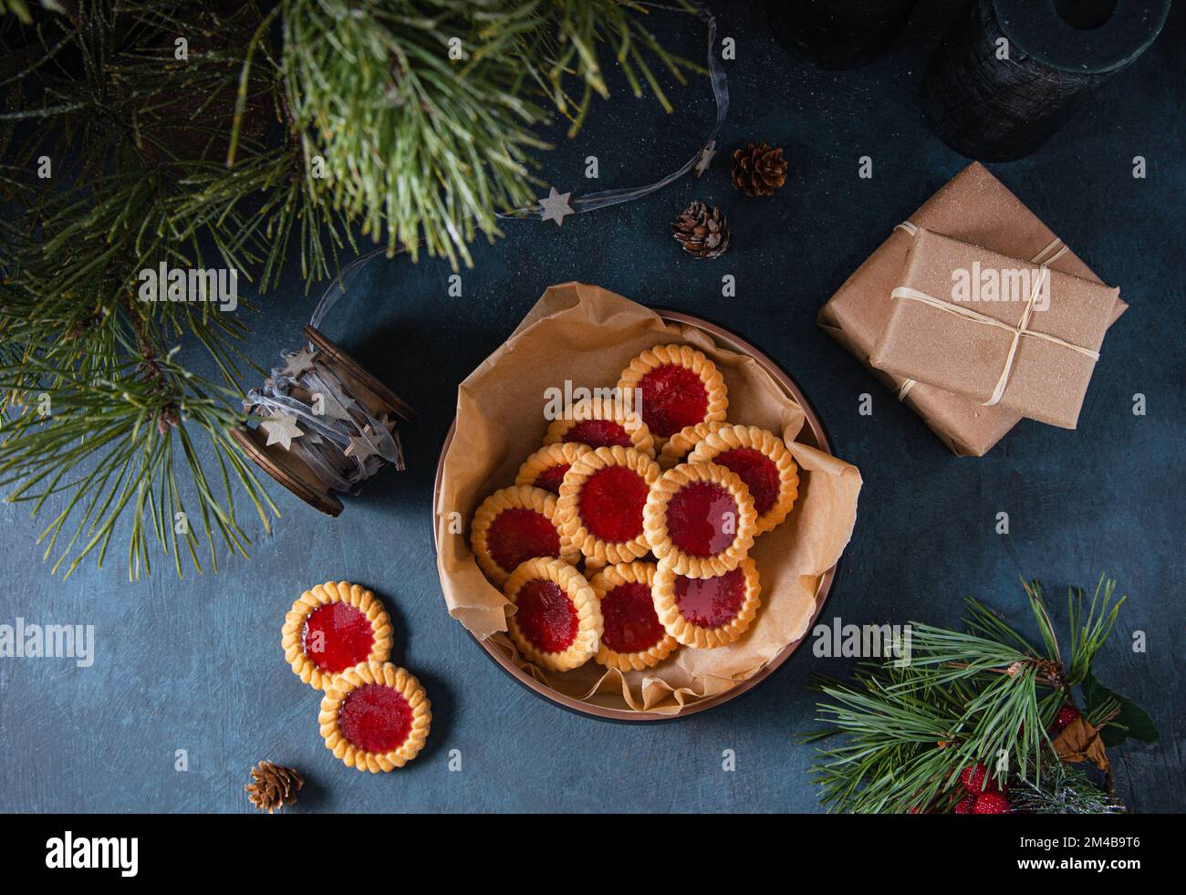 Biscotti fatti in casa con marmellata di frutta in una ciotola su un tavolo blu scuro con scatola presente e abete. Immagine scura e di umore. Vista dall'alto Foto Stock