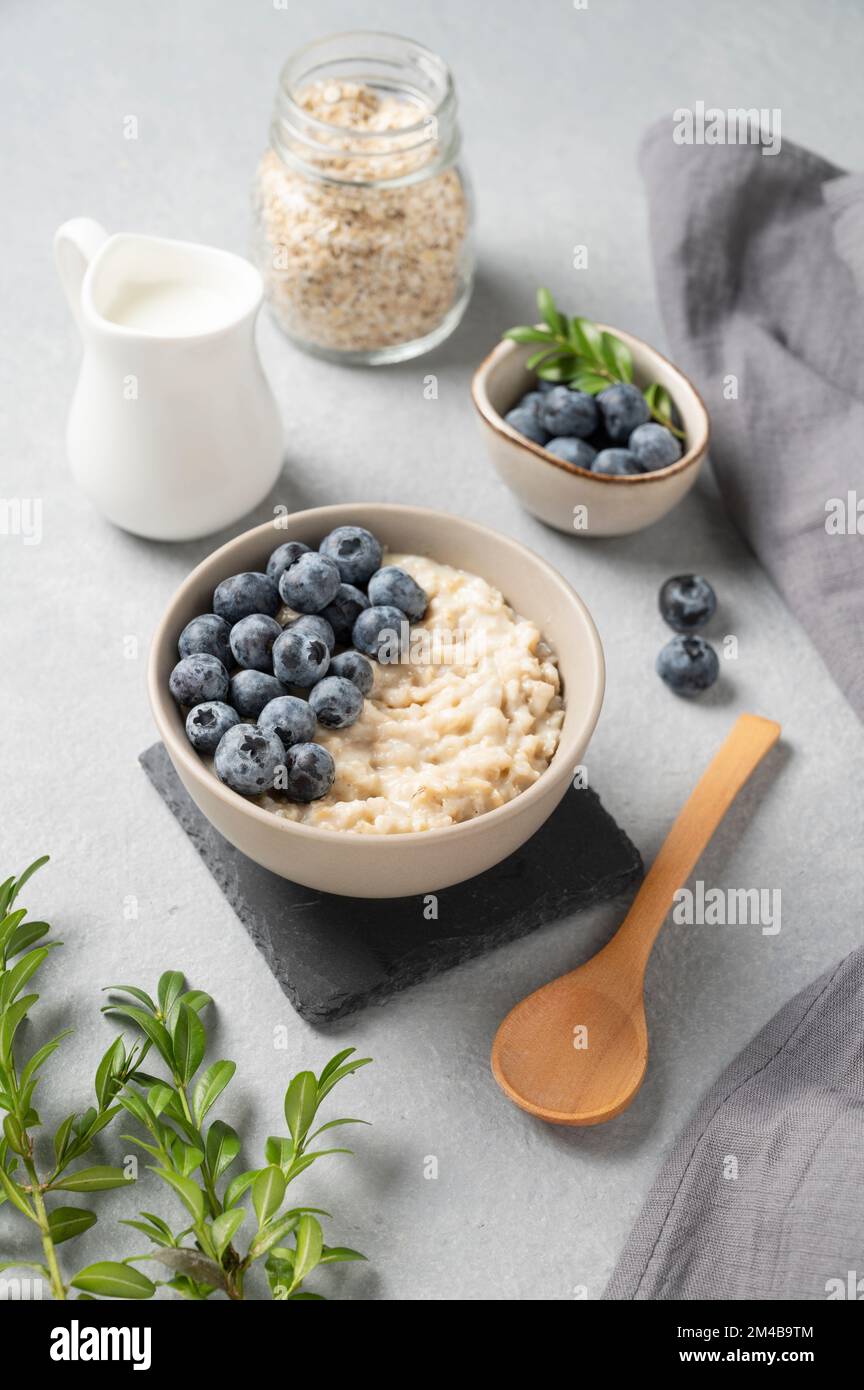 Porridge di farina d'avena con mirtilli in ciotola su fondo blu con bacche e latte. Il concetto di una colazione deliziosa, nutriente e sana. Foto Stock