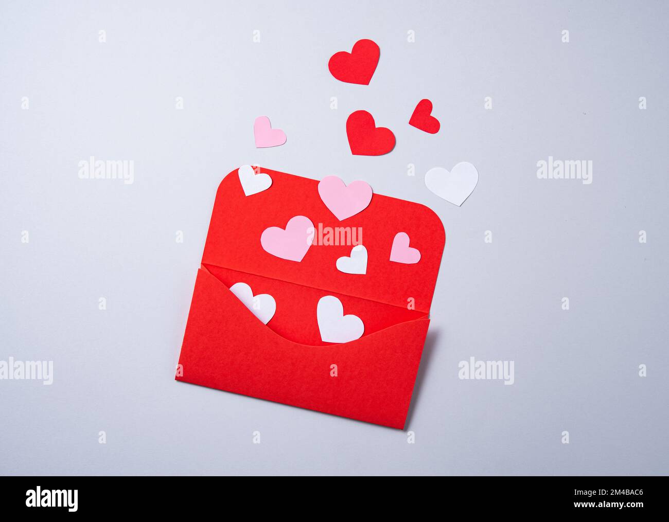 I cuori di carta rossa, rosa e bianca escono dalla busta rossa su sfondo grigio. Il concetto di San Valentino. Disposizione piatta, spazio di copia e vista dall'alto. Foto Stock
