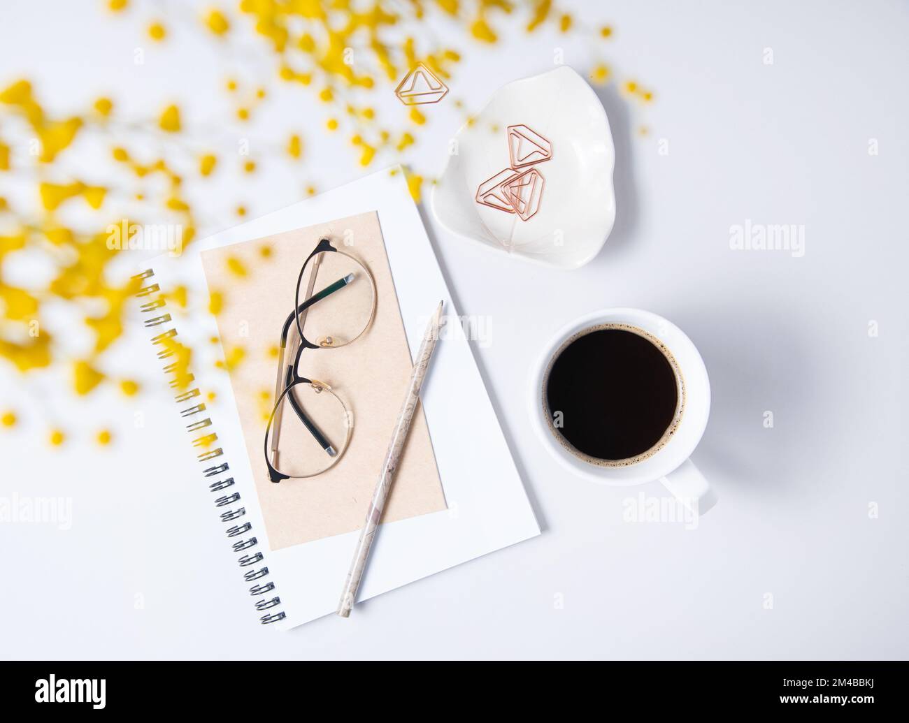 Piatto con fiore mimosa giallo, tazza di caffè, bicchieri, un quaderno artigianale su un tavolo di marmo. Desktop floreale da donna. concetto di mattina. top vie Foto Stock