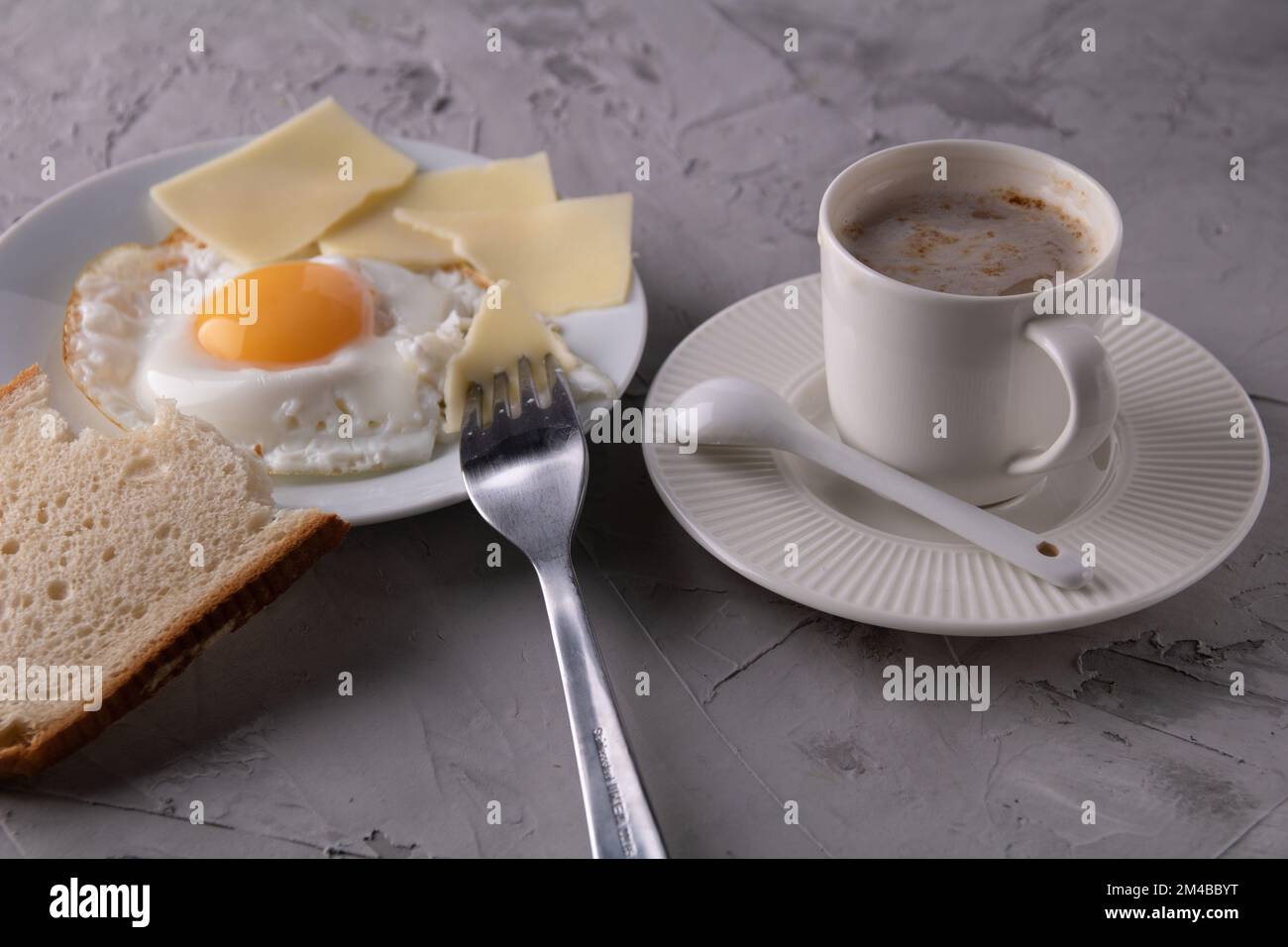 foto uovo con formaggio e pane su un piatto accanto ad una tazza leggera di caffè su un piattino, sul piattino c'è un cucchiaio Foto Stock