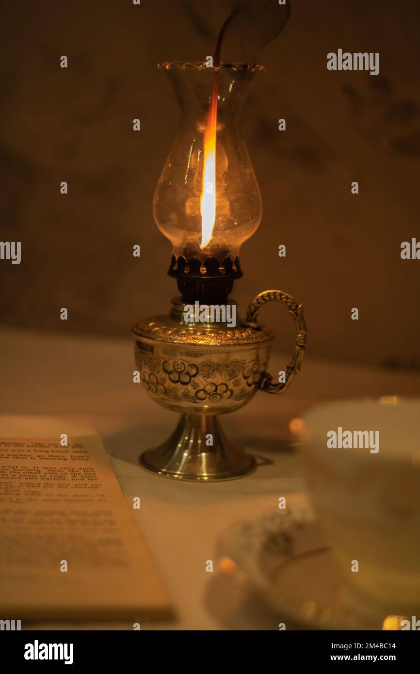 foto una tazza retrò vuota e un piattino si trova accanto ad un vecchio libro aperto e ad una lampada al cherosene che brucia Foto Stock