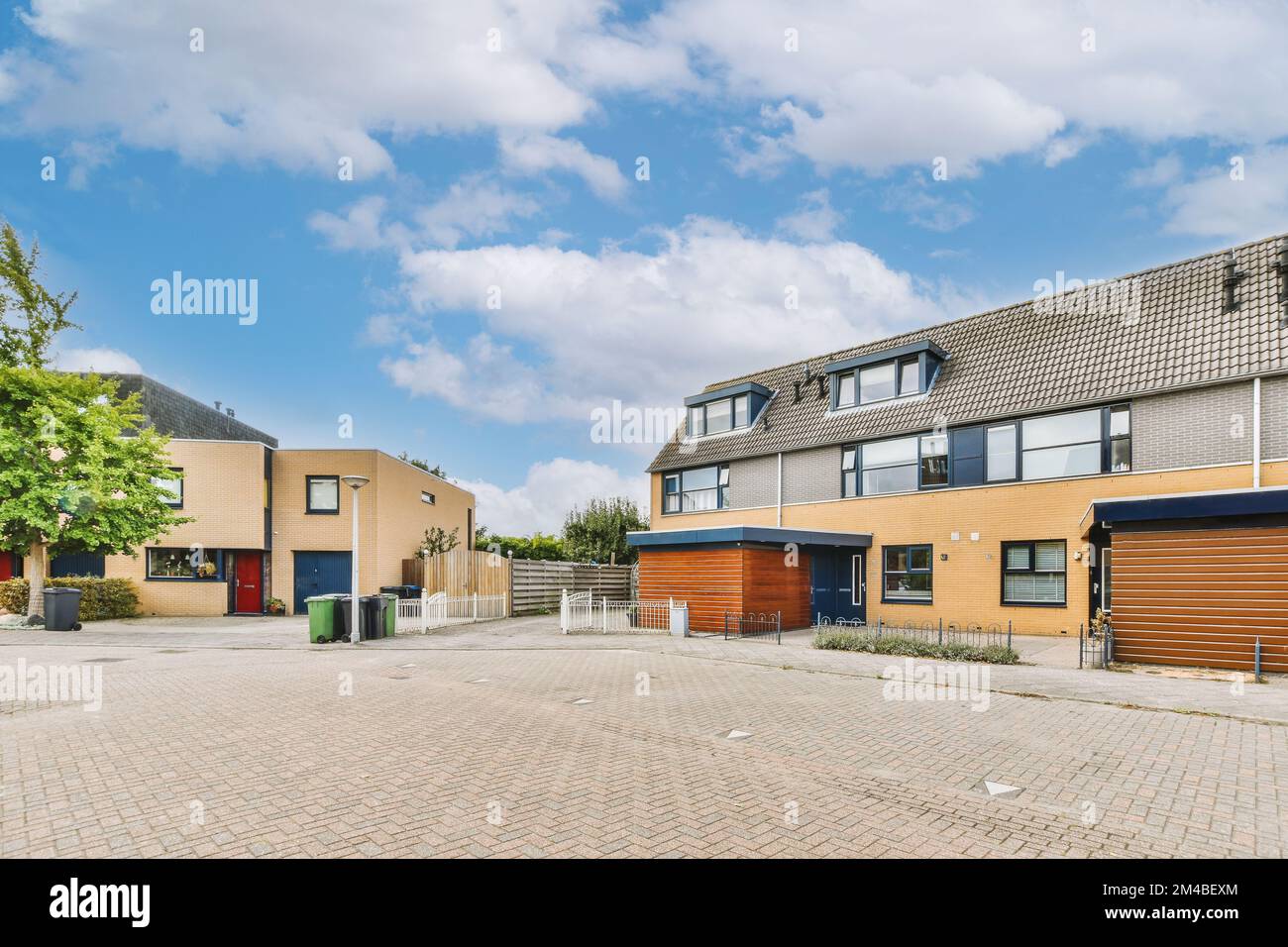 un parcheggio vuoto al centro di una zona residenziale con case e alberi su entrambi i lati, sotto un cielo blu Foto Stock