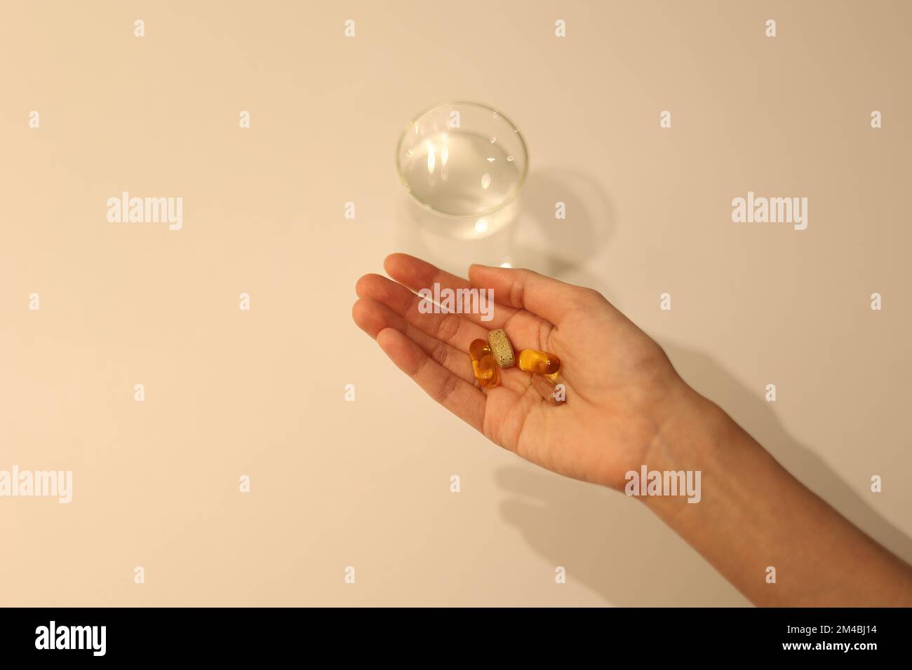 La donna sta prendendo la medicina con la tazza di acqua sulla tabella bianca, la ragazza sta prendendo il supplemento nutrizionale a mano Foto Stock