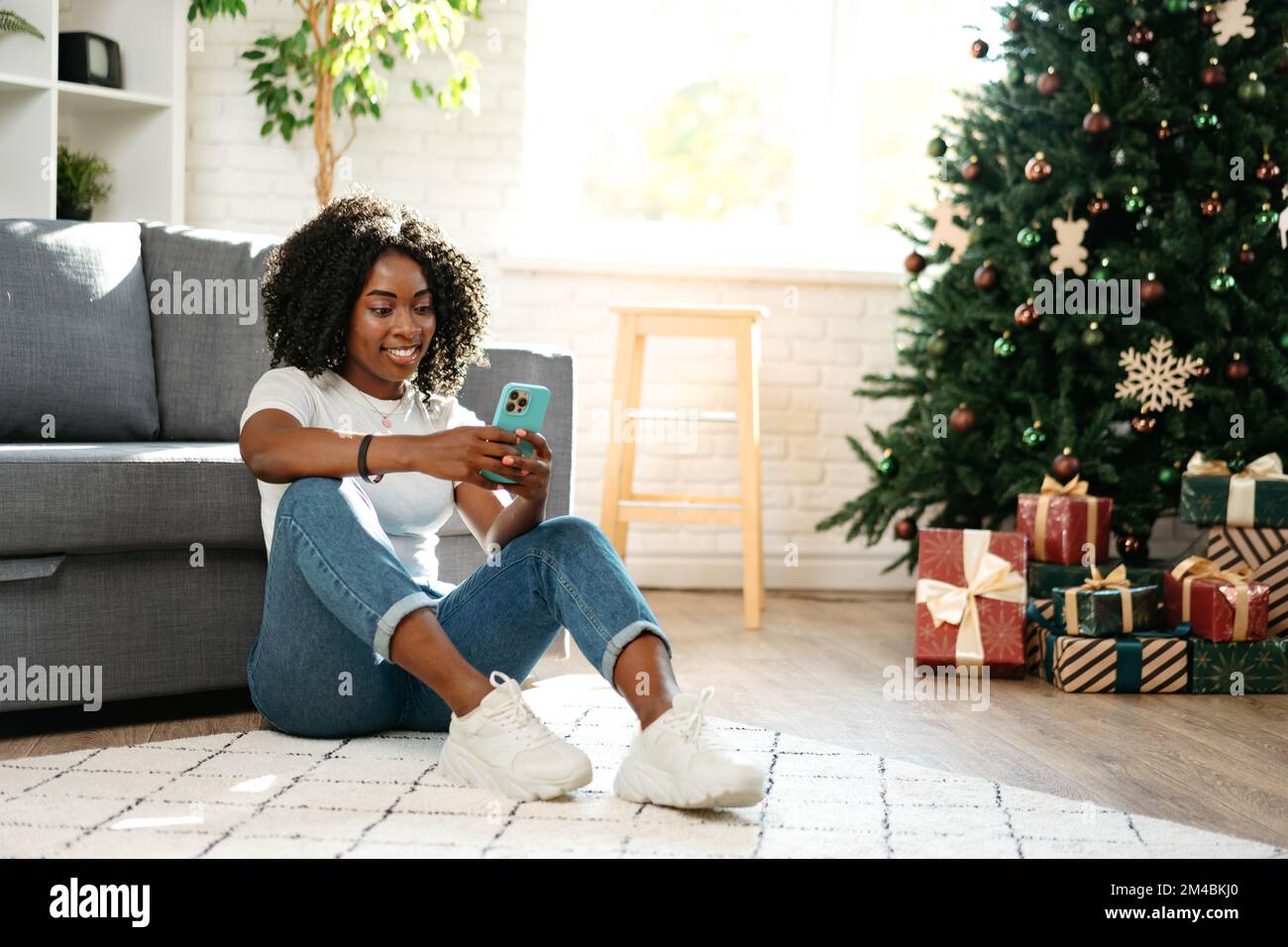 Felice donna nera che usa lo smartphone in una stanza decorata per Natale Foto Stock