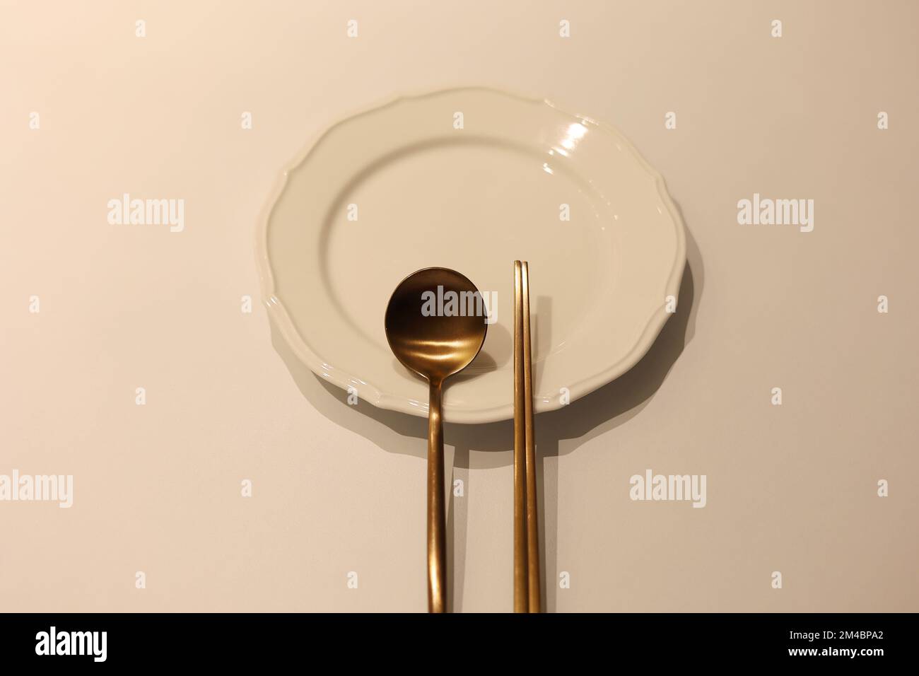 Un set di cucchiaio e bastone di ottone coreano con piatto bianco vuoto sul tavolo Foto Stock