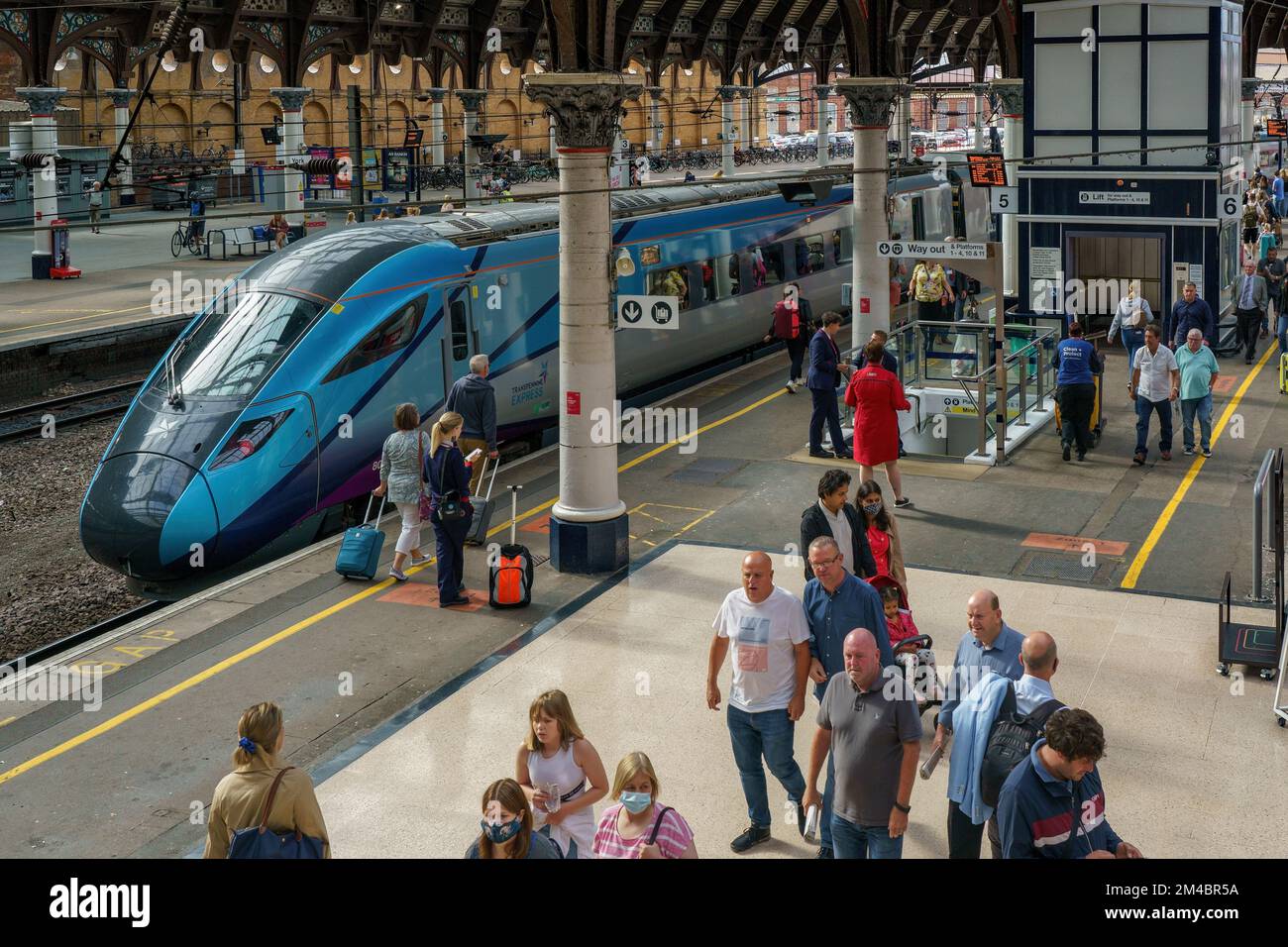 I viaggiatori in treno che camminano lungo York Un treno Transpennine Express di colore azzurro si ferma sul binario della stazione ferroviaria di York, York, Regno Unito. Foto Stock