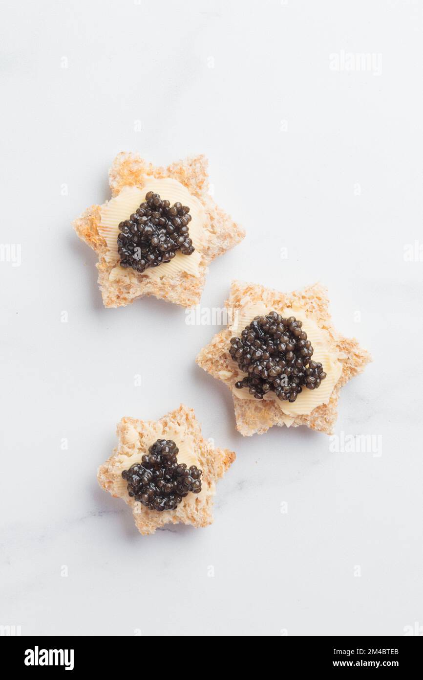Antipasti neri al caviale stelle del pane con burro su sfondo bianco vista dall'alto verticale Foto Stock