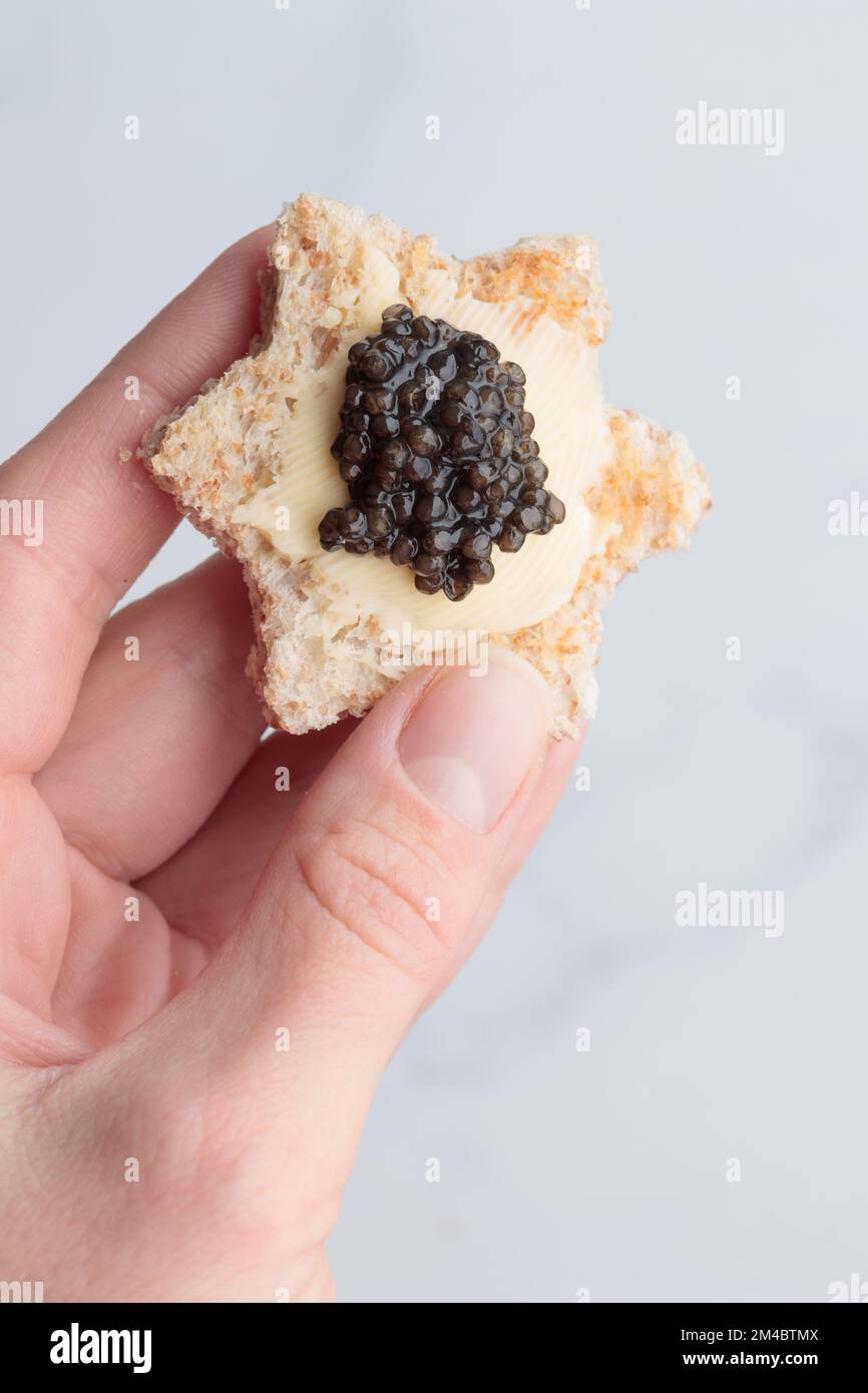 Antipasti neri al caviale stelle del pane con burro in mano umana su sfondo bianco vista dall'alto verticale Foto Stock
