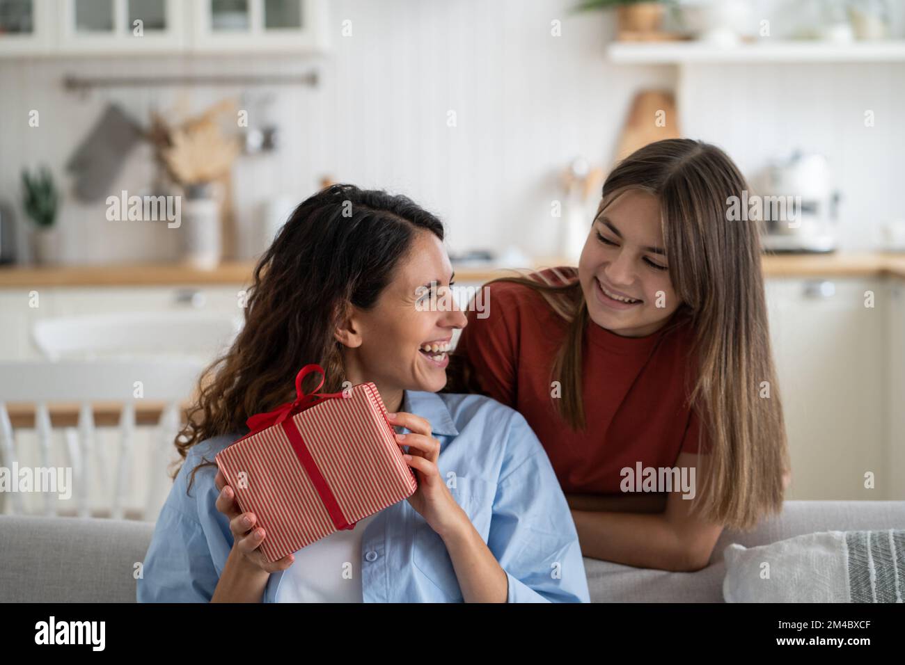 Ridendo soddisfatto babysitter donna ha ricevuto il regalo dalla ragazza teenage stand vicino al divano in soggiorno Foto Stock