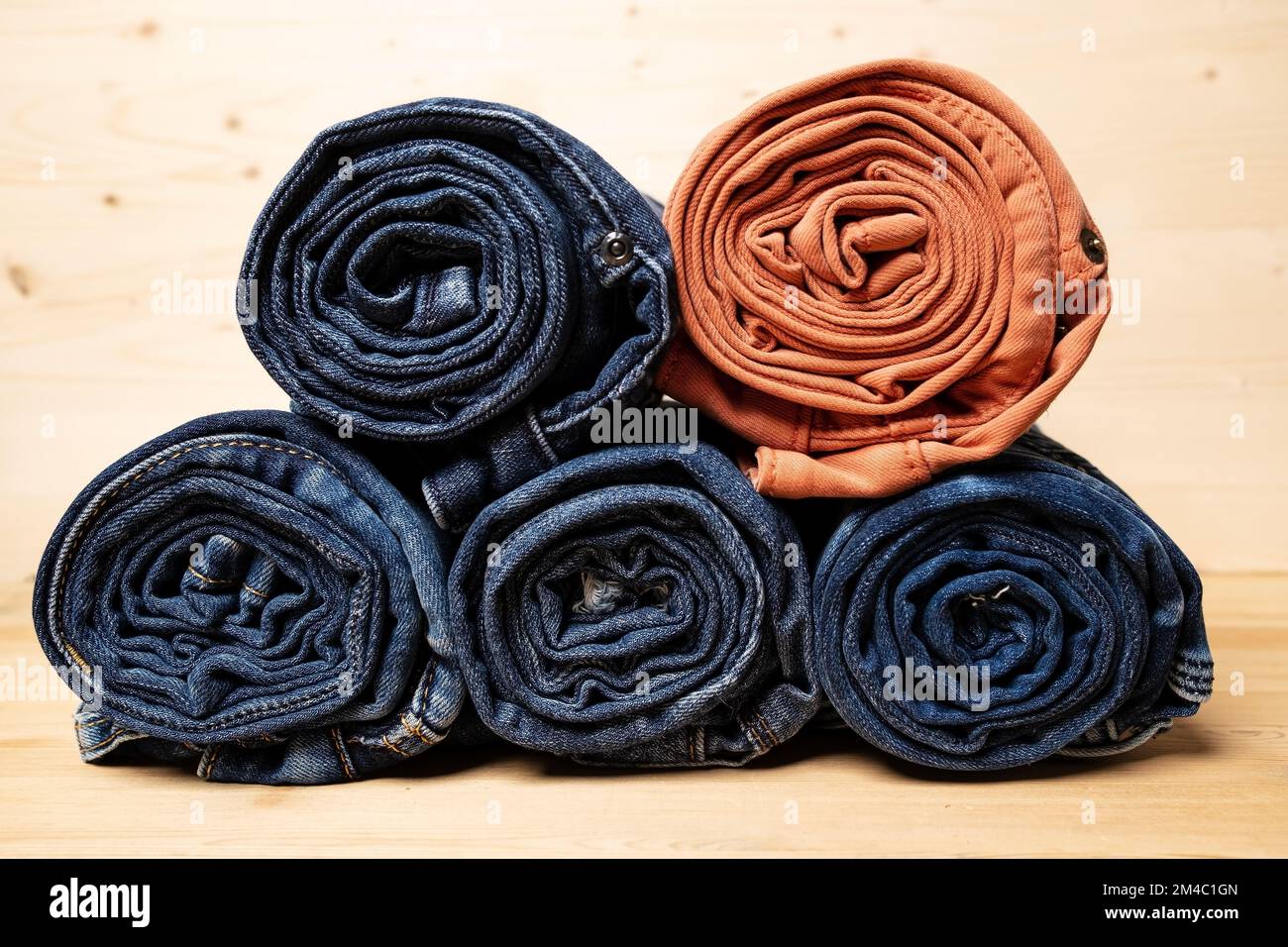 I jeans sono arrotolati e impilati, su uno sfondo di legno. Foto Stock