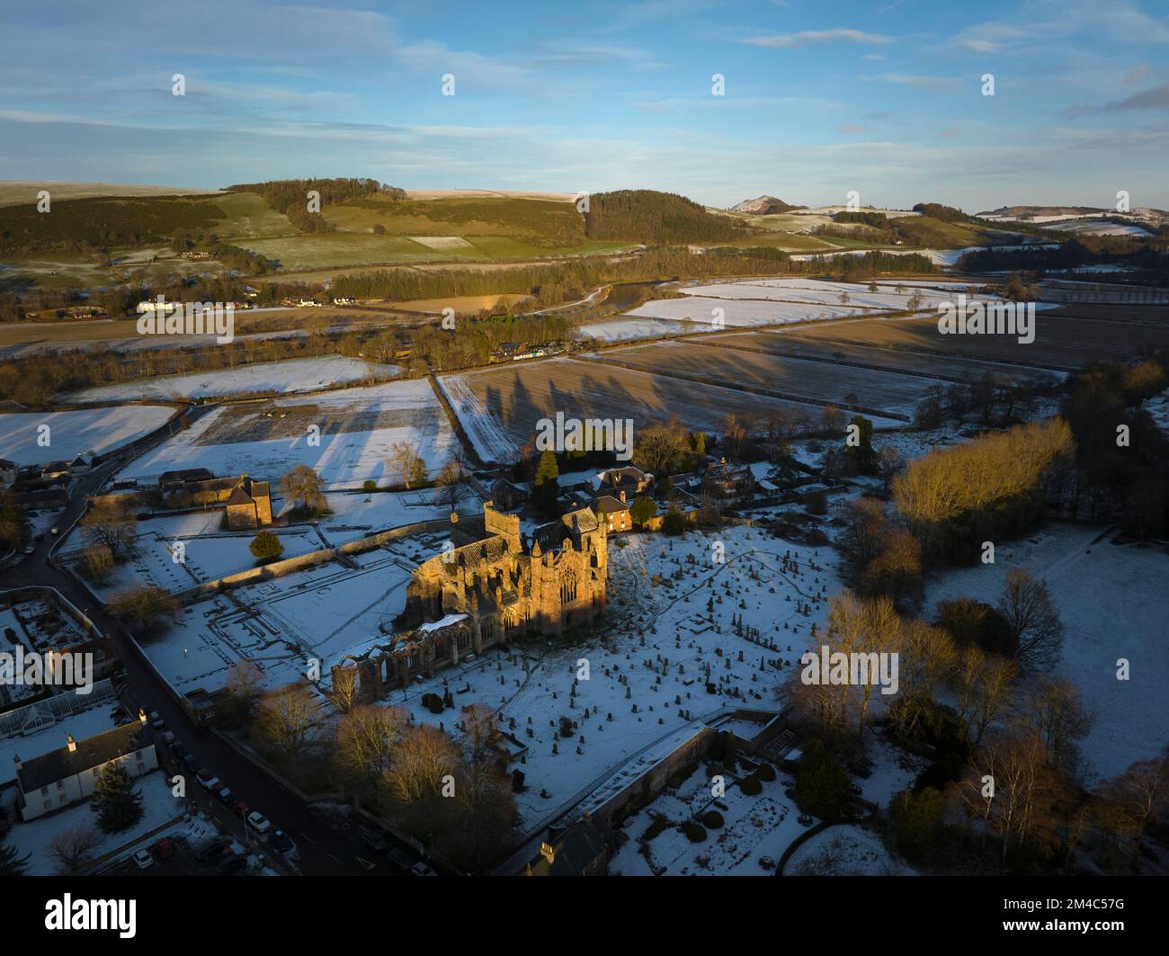 Ripresa aerea dell'Abbazia di Melrose e della Casa del Comendatore con uno strato di neve e gelo al tramonto in una frizzante giornata invernale a dicembre. Foto Stock