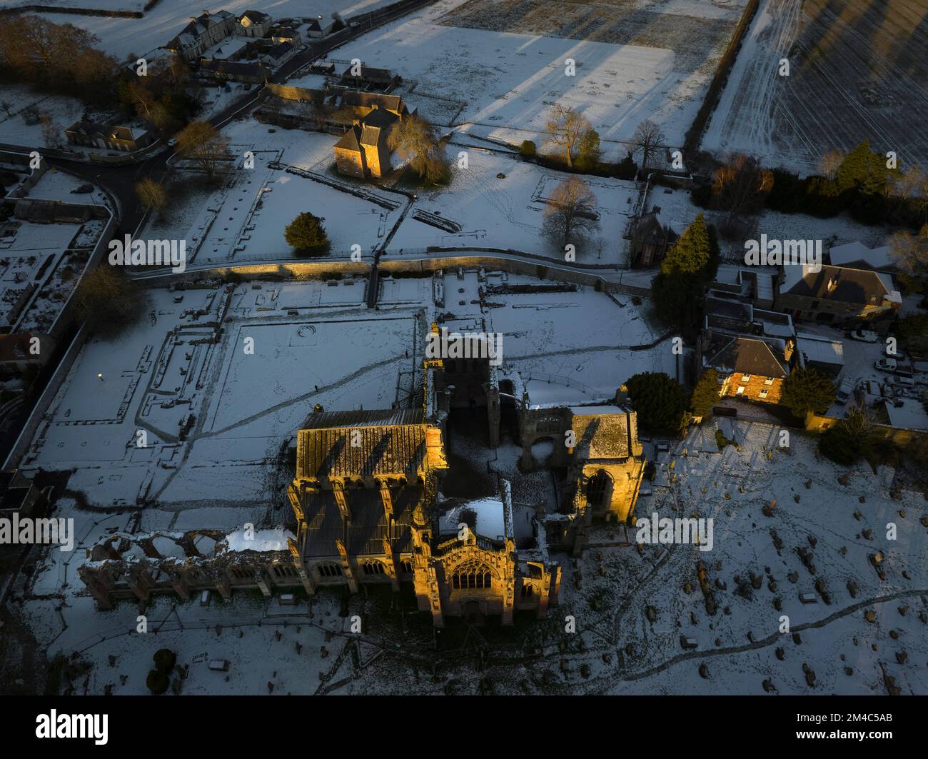 Ripresa aerea dell'Abbazia di Melrose e della Casa del Comendatore con uno strato di neve e gelo al tramonto in una frizzante giornata invernale a dicembre. Foto Stock