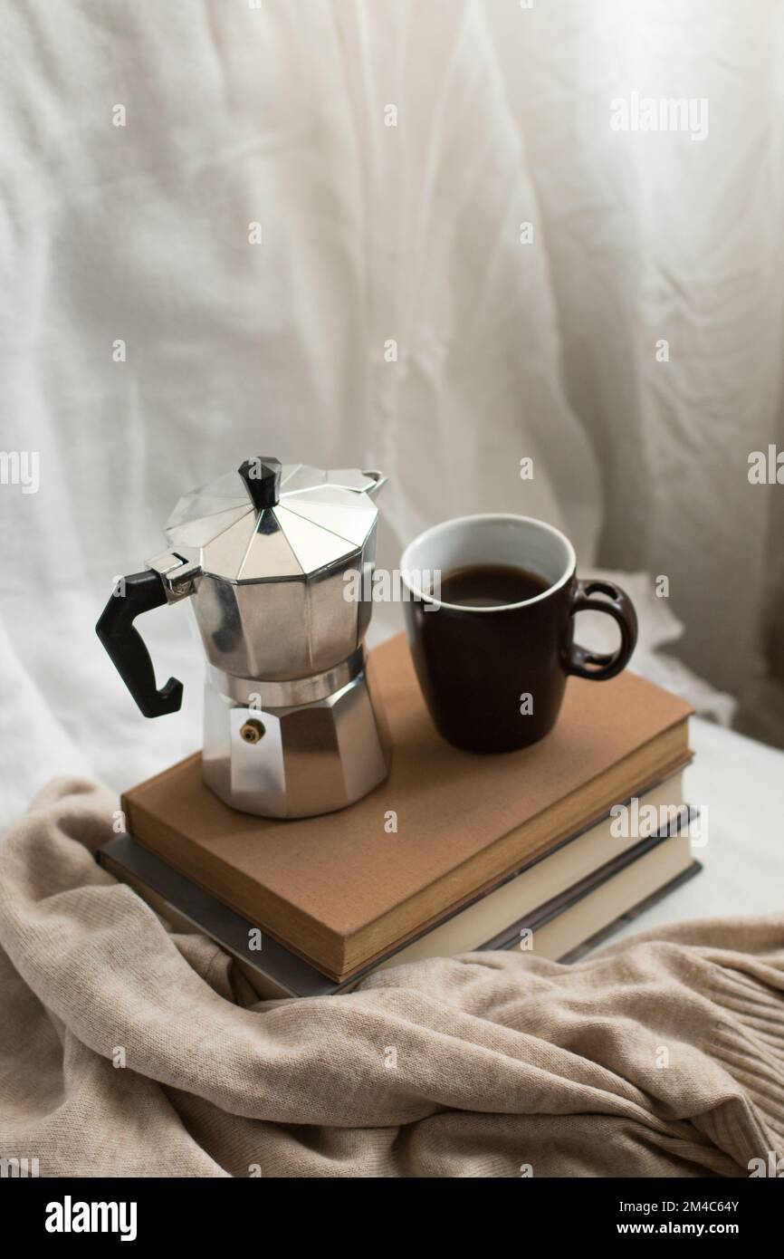Una tazza di caffè e una moka pot su alcuni libri in uno spazio