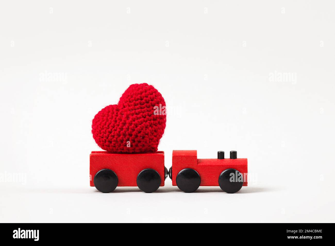 Treno rosso con cuore lavorato a maglia rosso su sfondo grigio. San Valentino, simbolo dell'amore. Foto Stock