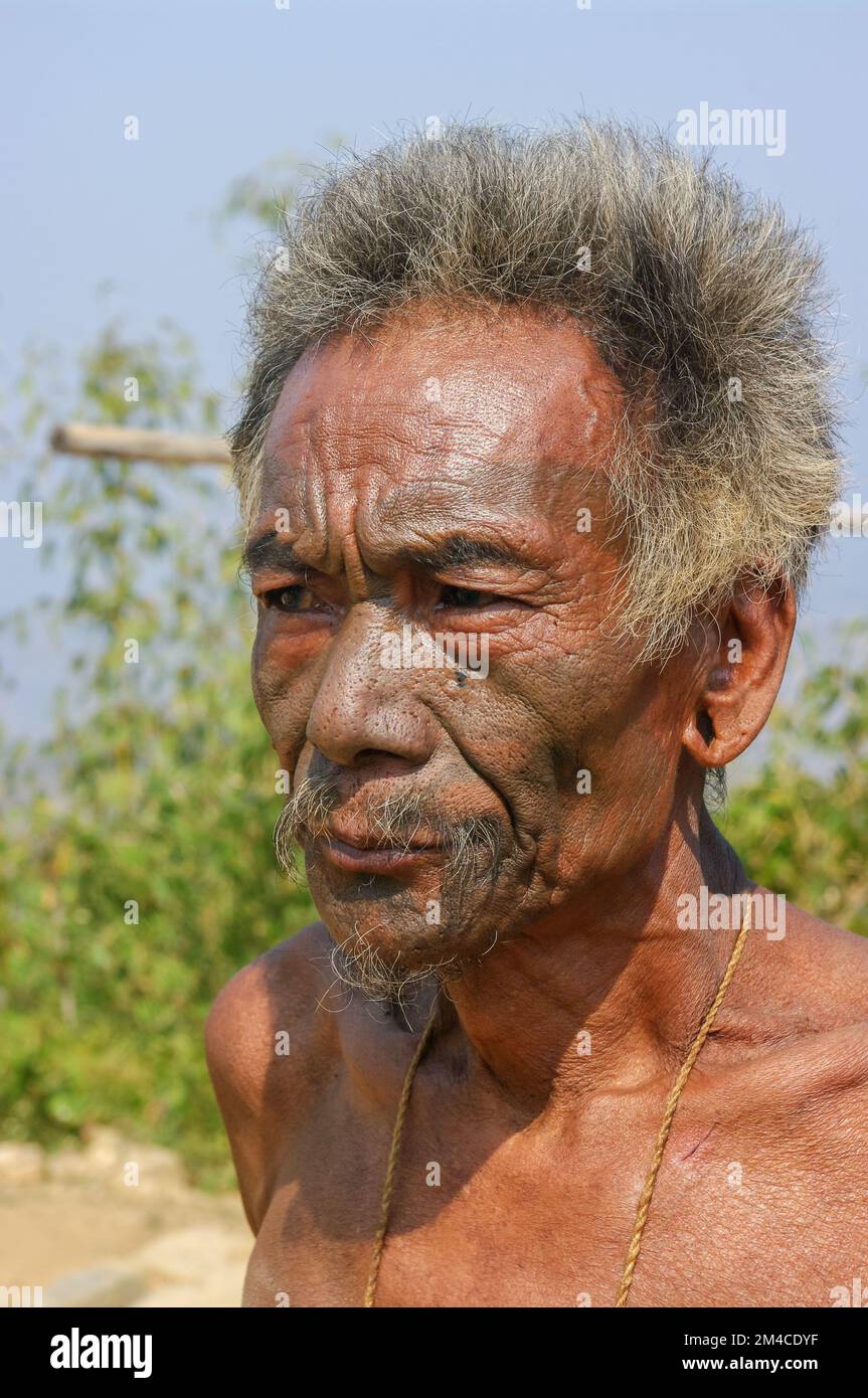 Mon, Nagaland, India - 02 27 2013 : Ritratto all'aperto della vecchia tribù Naga Konyak cacciatore capo guerriero con tatuaggio facciale tradizionale su sfondo naturale Foto Stock