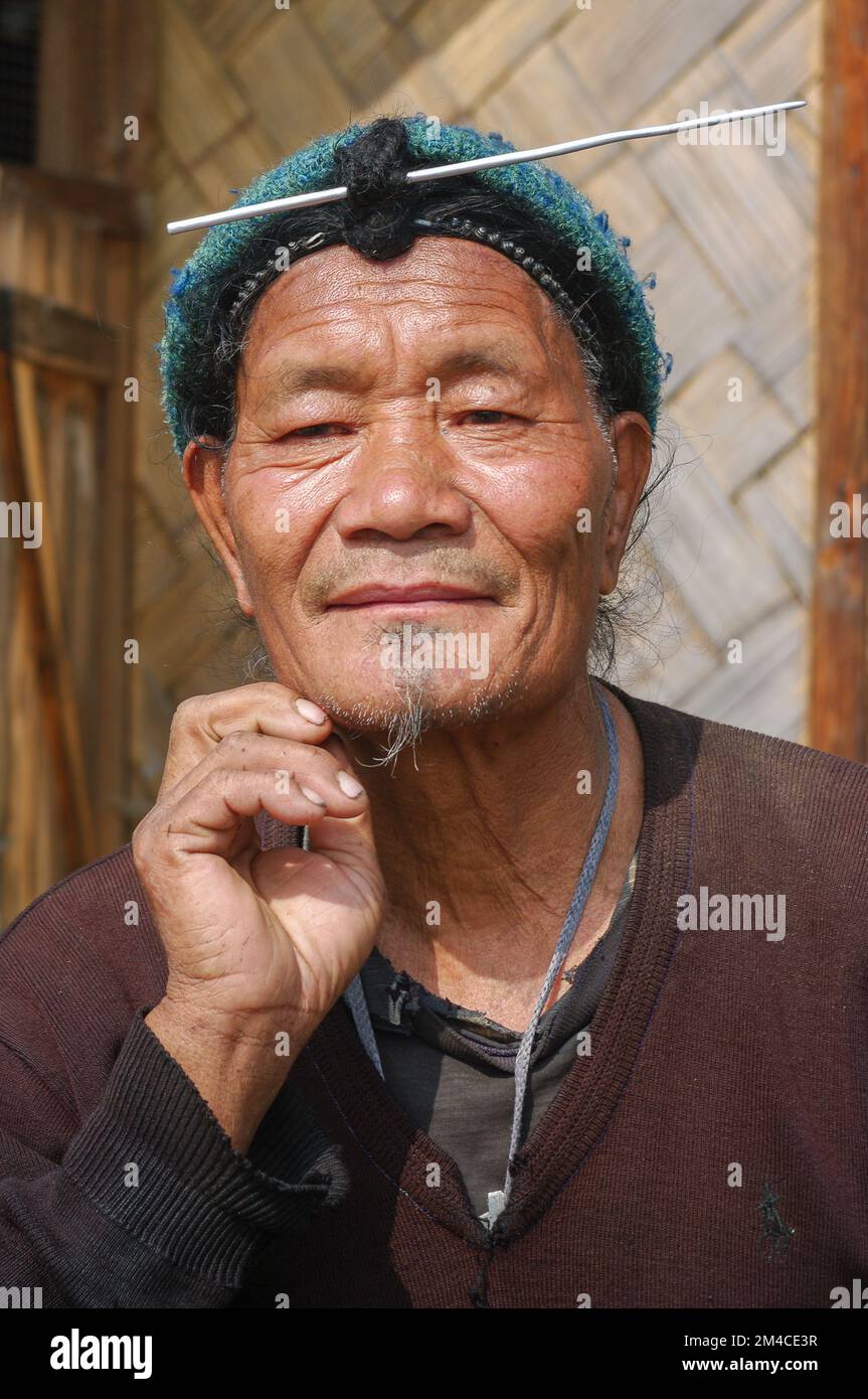 Ziro, Arunachal Pradesh, India - 03 04 2014 : Ritratto dell'uomo tribale di mezza età Apatani con tradizionale pancia anteriore per capelli e ago che indossa una capsula blu Foto Stock