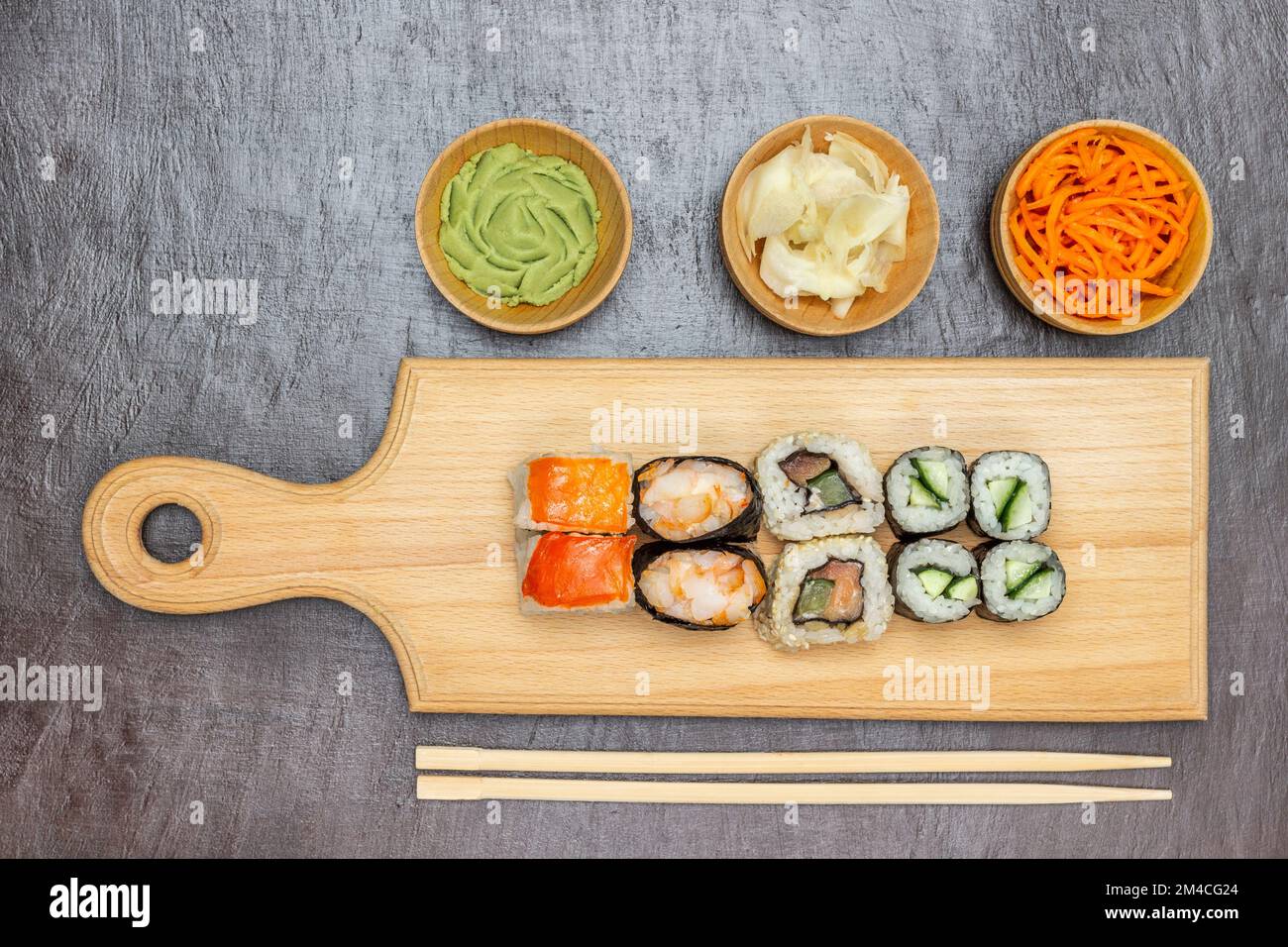 Sushi su un tagliere. Chopsticks sul tavolo. Wasabi, zenzero sottaceto e carote in ciotole. Giacitura piatta. Sfondo marrone. Foto Stock