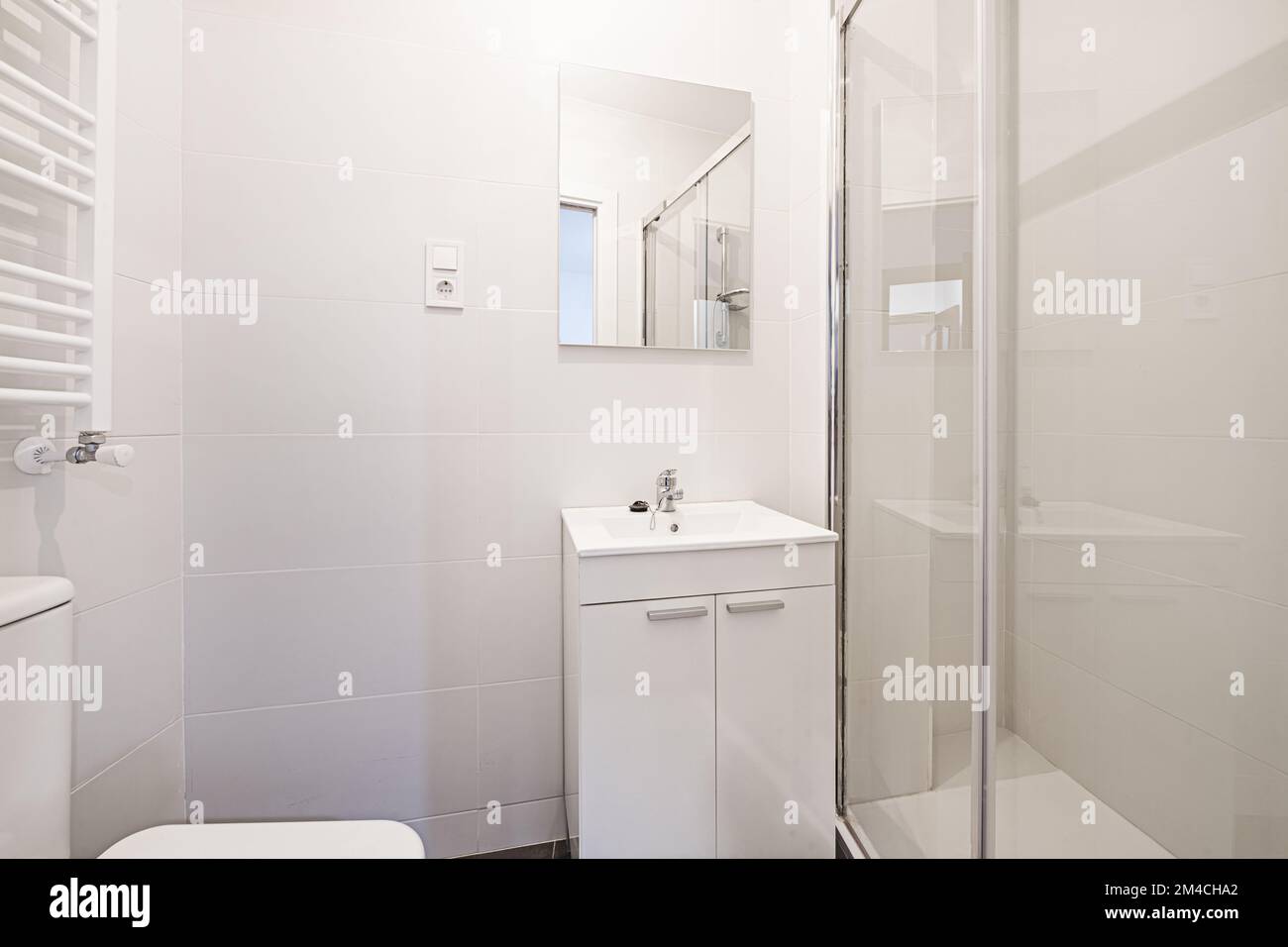 Piccolo bagno con armadio a muro in legno laccato bianco con porte, specchio quadrato senza cornice e cabina doccia con schermo in vetro trasparente Foto Stock