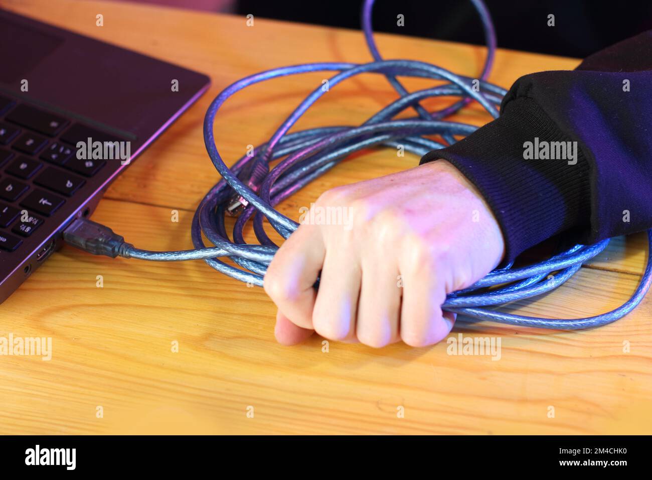 tirando con forza il cavo usb blu dal computer portatile da una persona in una felpa nera Foto Stock