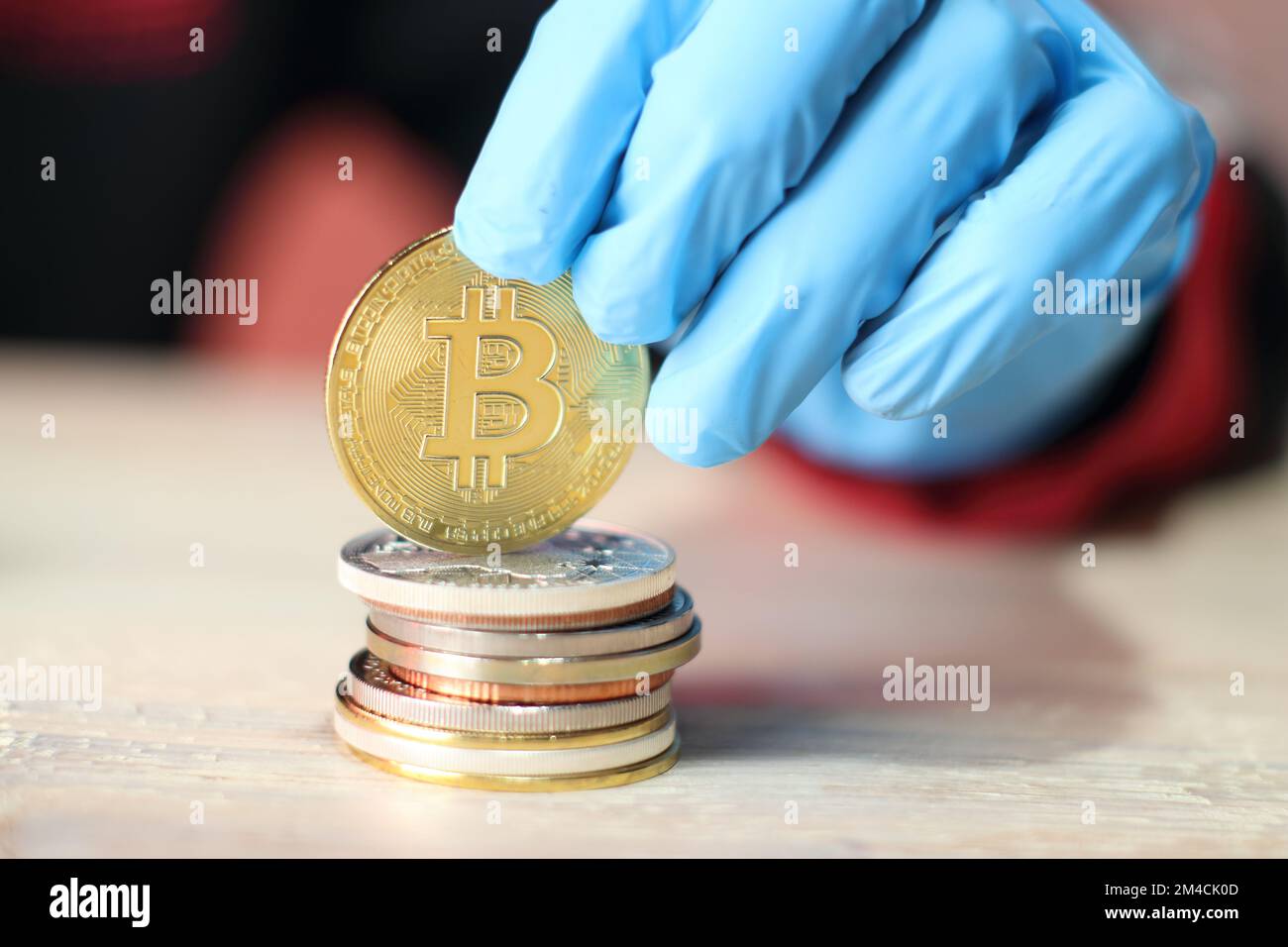 moneta bitcoin tenuta su un mucchio di monete da una persona che indossa  guanti blu contro una parete colorata Foto stock - Alamy