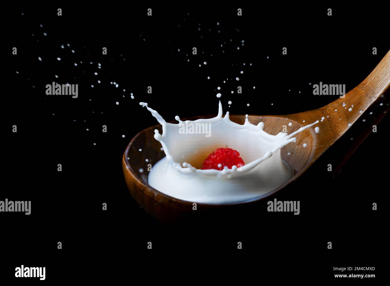 lampone spruzzando latte su un cucchiaio di legno, su sfondo nero Foto Stock