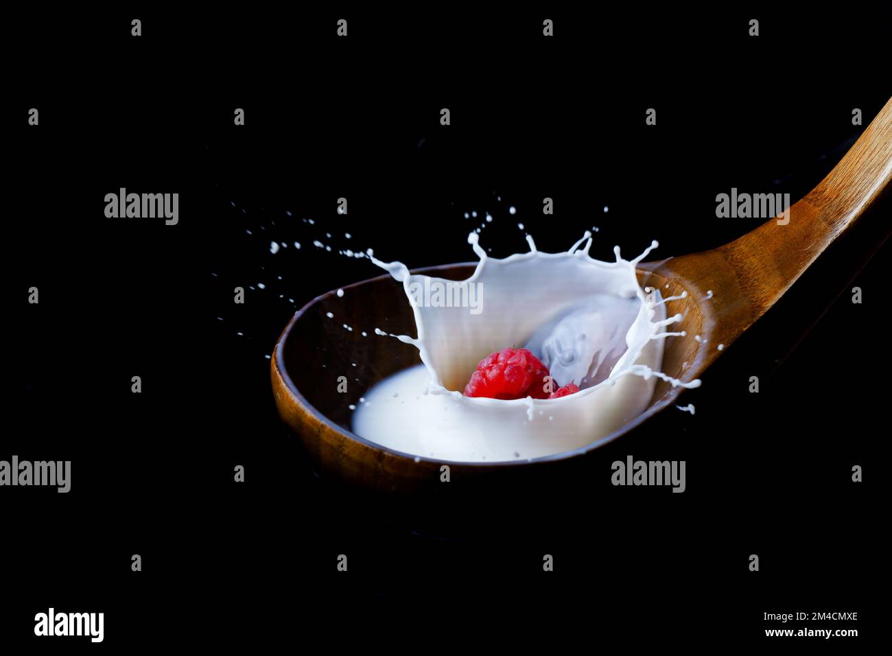 lampone spruzzando latte su un cucchiaio di legno, su sfondo nero Foto Stock