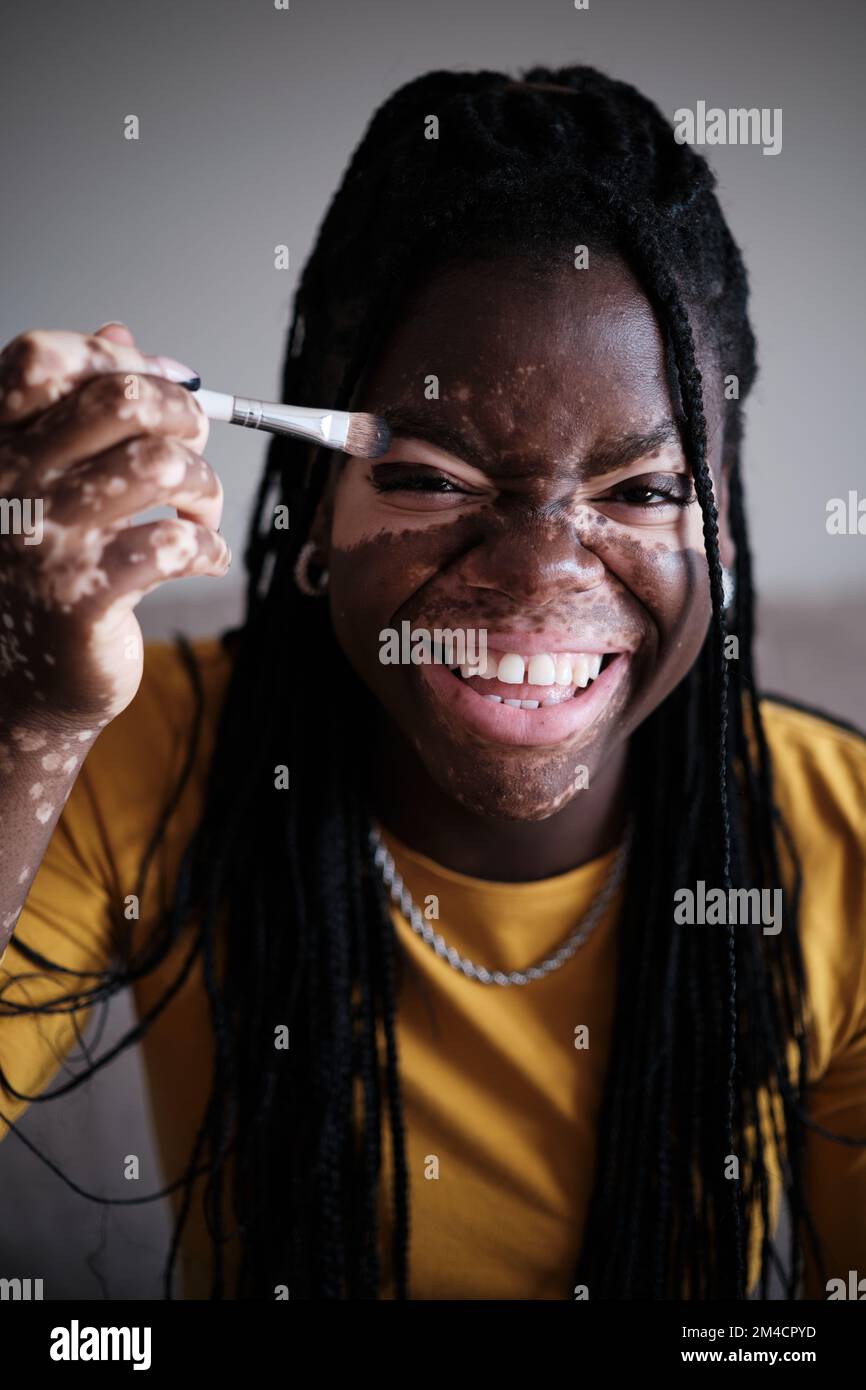 Donna nera positiva con pigmentazione bianca ridendo mentre fa il trucco Foto Stock