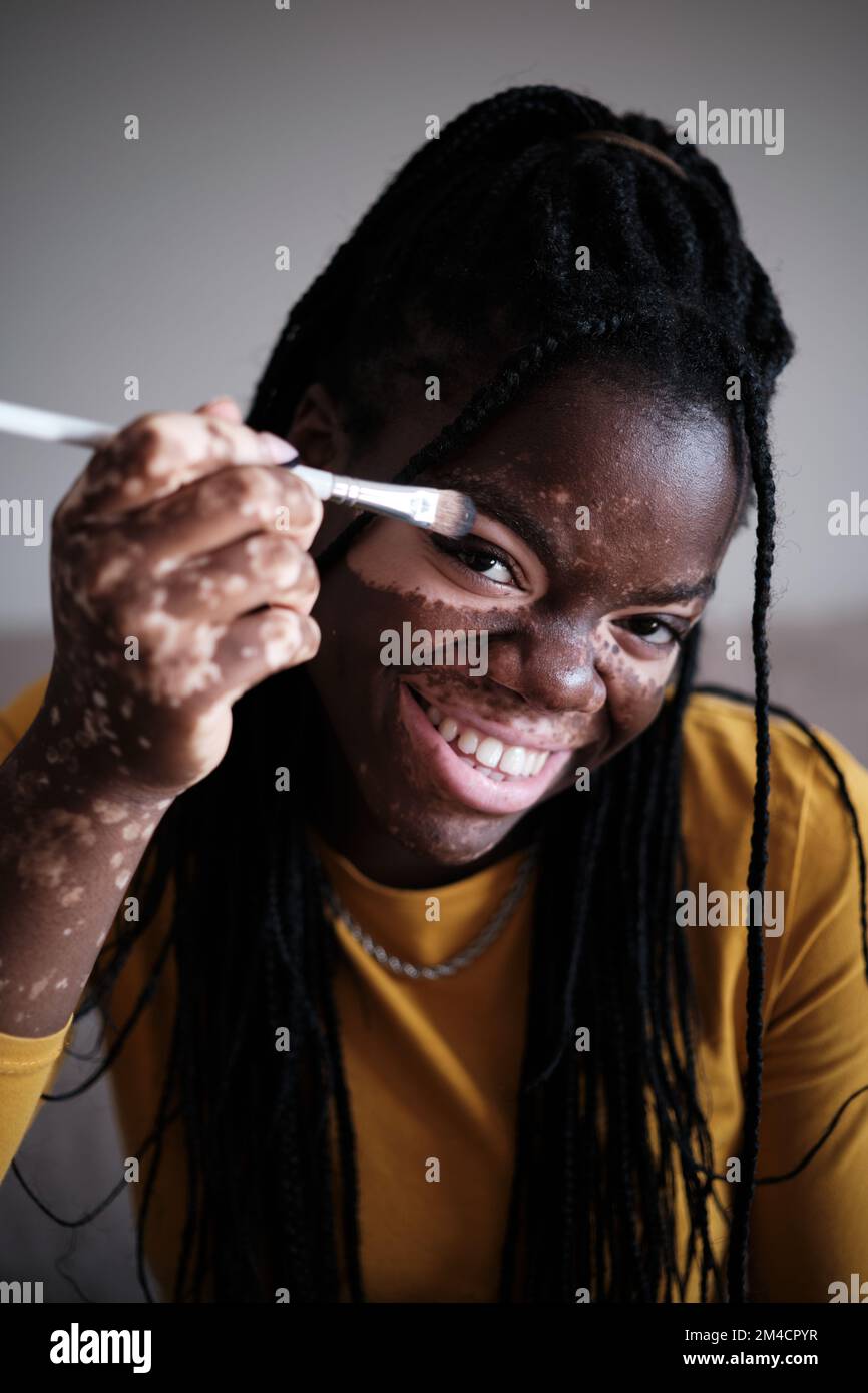 Donna nera allegra con la pelle di vitiligo che fa il trucco Foto Stock