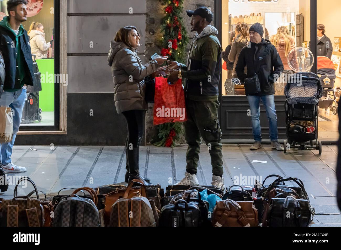 Napoli, Italia - 11 dicembre 2022: Una donna acquista una borsa da un venditore di strada, pagando in contanti. Foto Stock