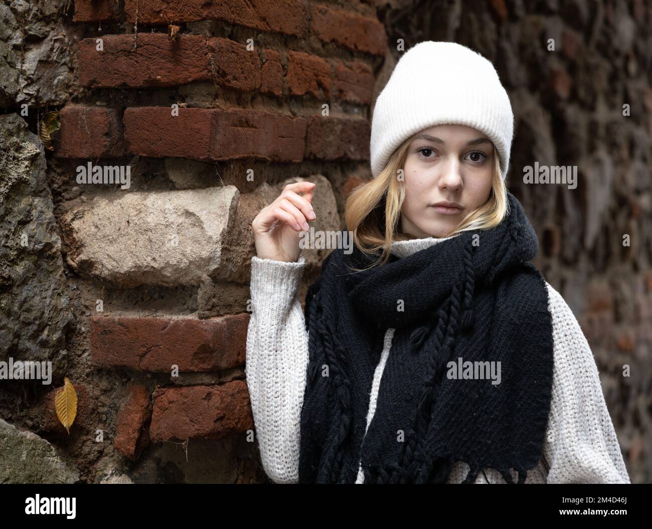 Una ragazza in abiti caldi e morbidi si trova vicino a un muro di mattoni e pietra testurizzati e guarda la macchina fotografica Foto Stock