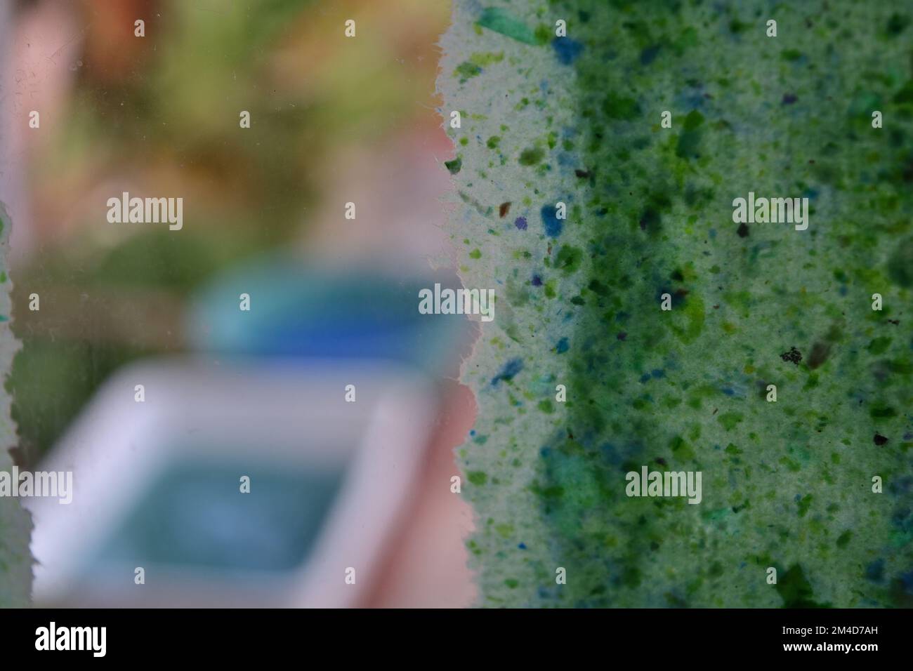 Foglio di carta riciclata che asciuga su una finestra di vetro e due bacini di plastica pieni di pasta di carta sullo sfondo. Foto Stock