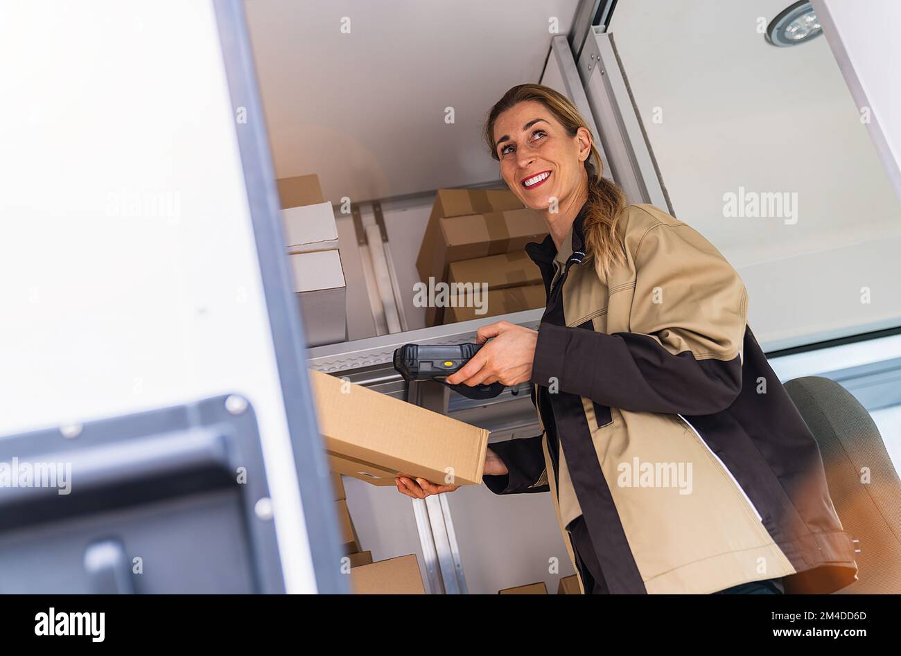 agente di consegna donna che scansiona il codice a barre con il lettore di codici a barre all'interno del furgone su un pacco Foto Stock