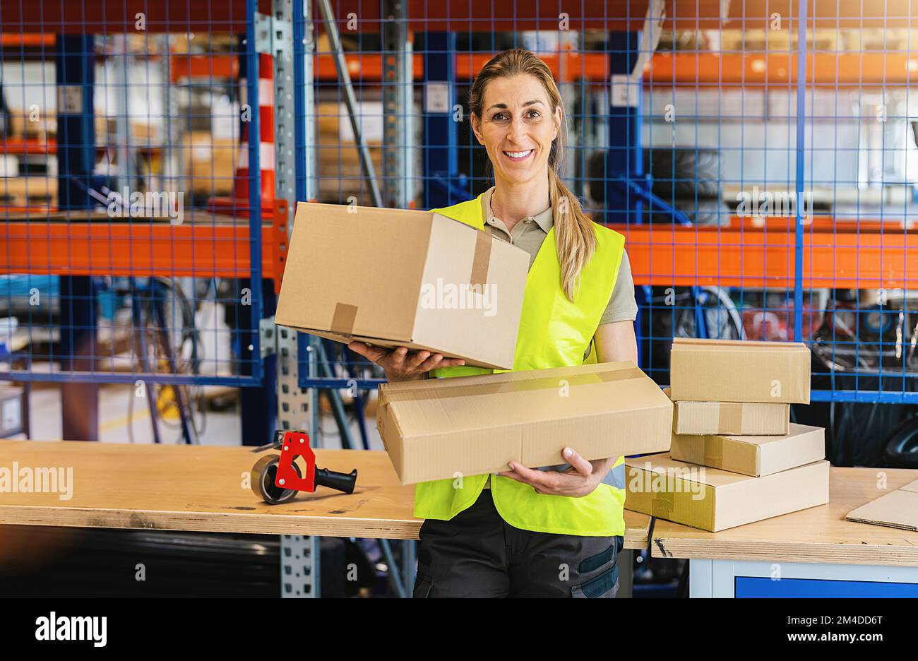 donna sorridente che tiene le casse di imballaggio dopo sigillarlo con nastro adesivo al magazzino dell'azienda di spedizione del trasporto Foto Stock