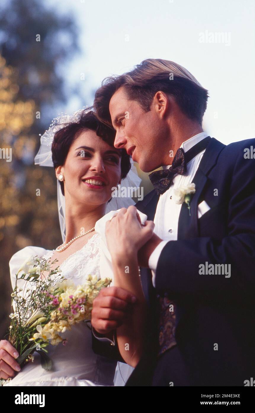 Giovane coppia caucasica abbracciando all'esterno al loro matrimonio guardandosi l'un l'altro Foto Stock